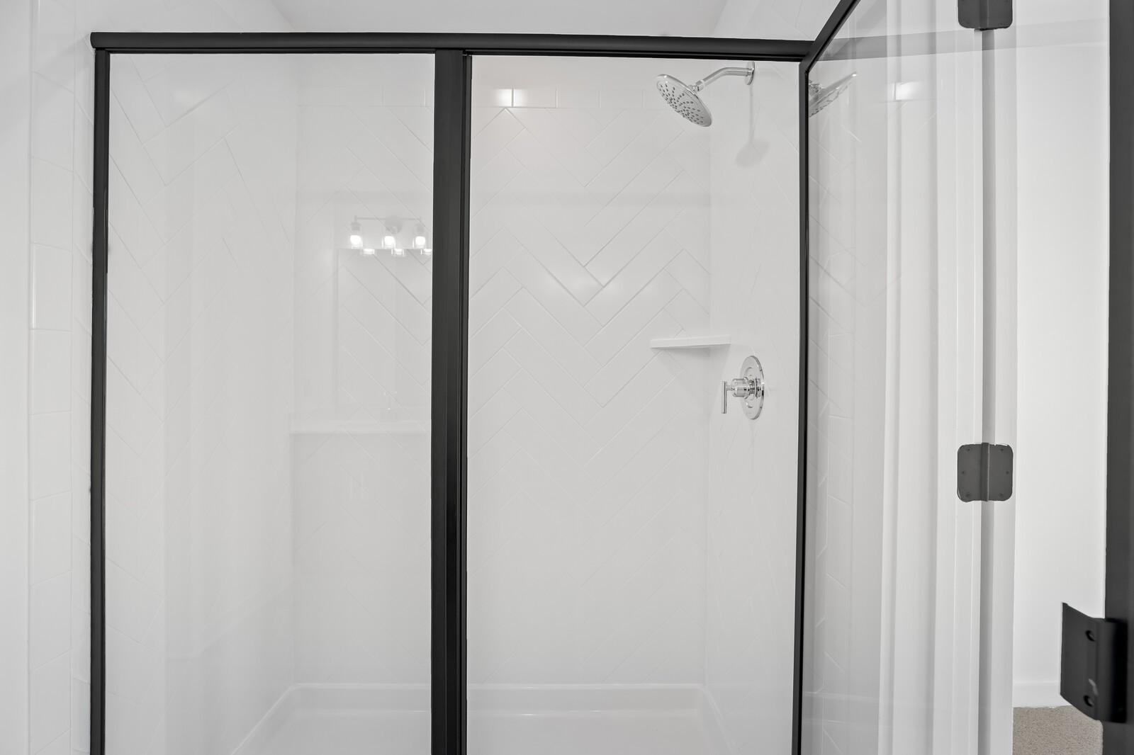 Modern frameless glass shower with black frames, herringbone white tile walls, and rainfall head in The Willow master bath, Gallatin, TN