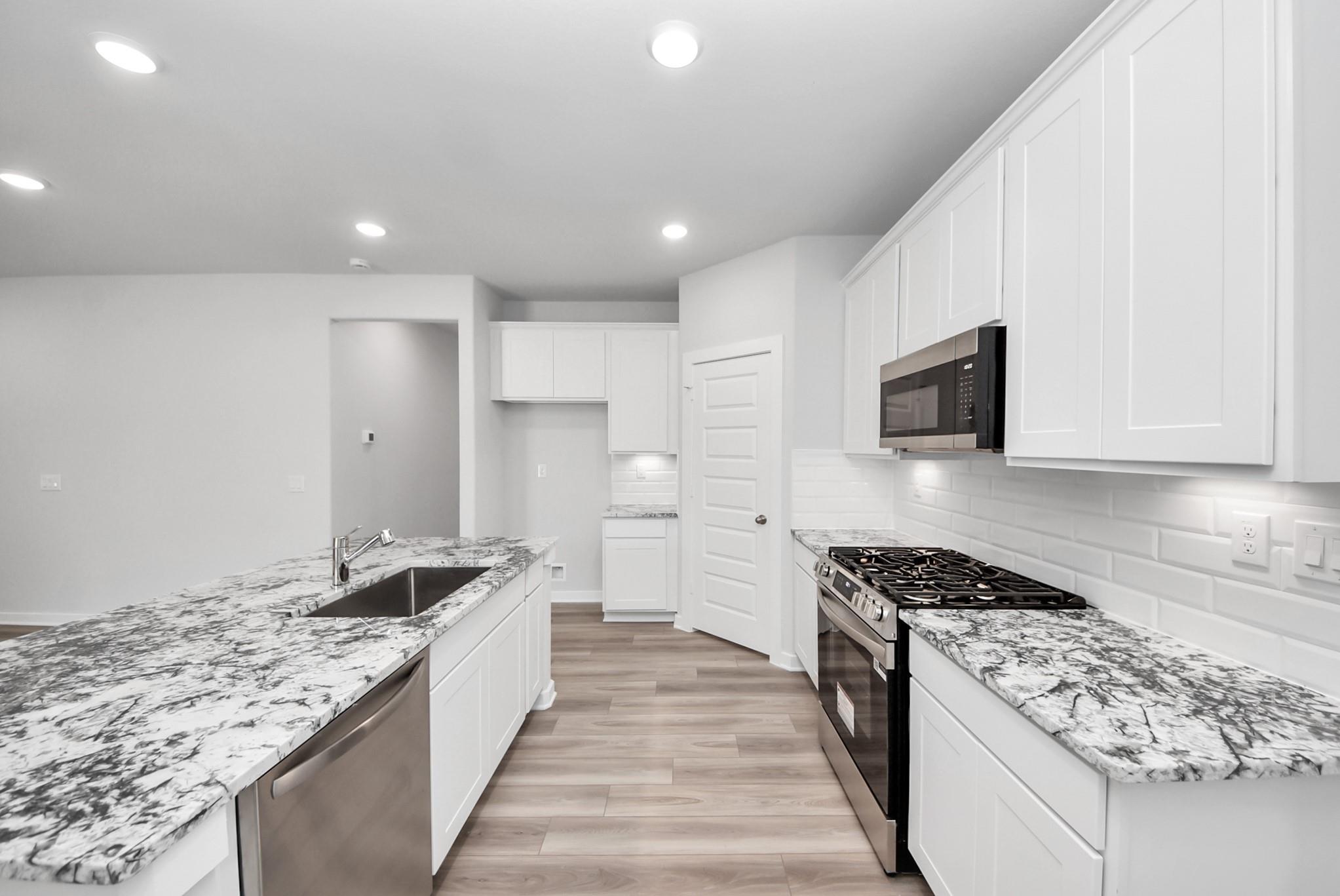Modern kitchen with white cabinets, granite countertops, and stainless appliances in The Sabine E floor plan, Magnolia, TX.