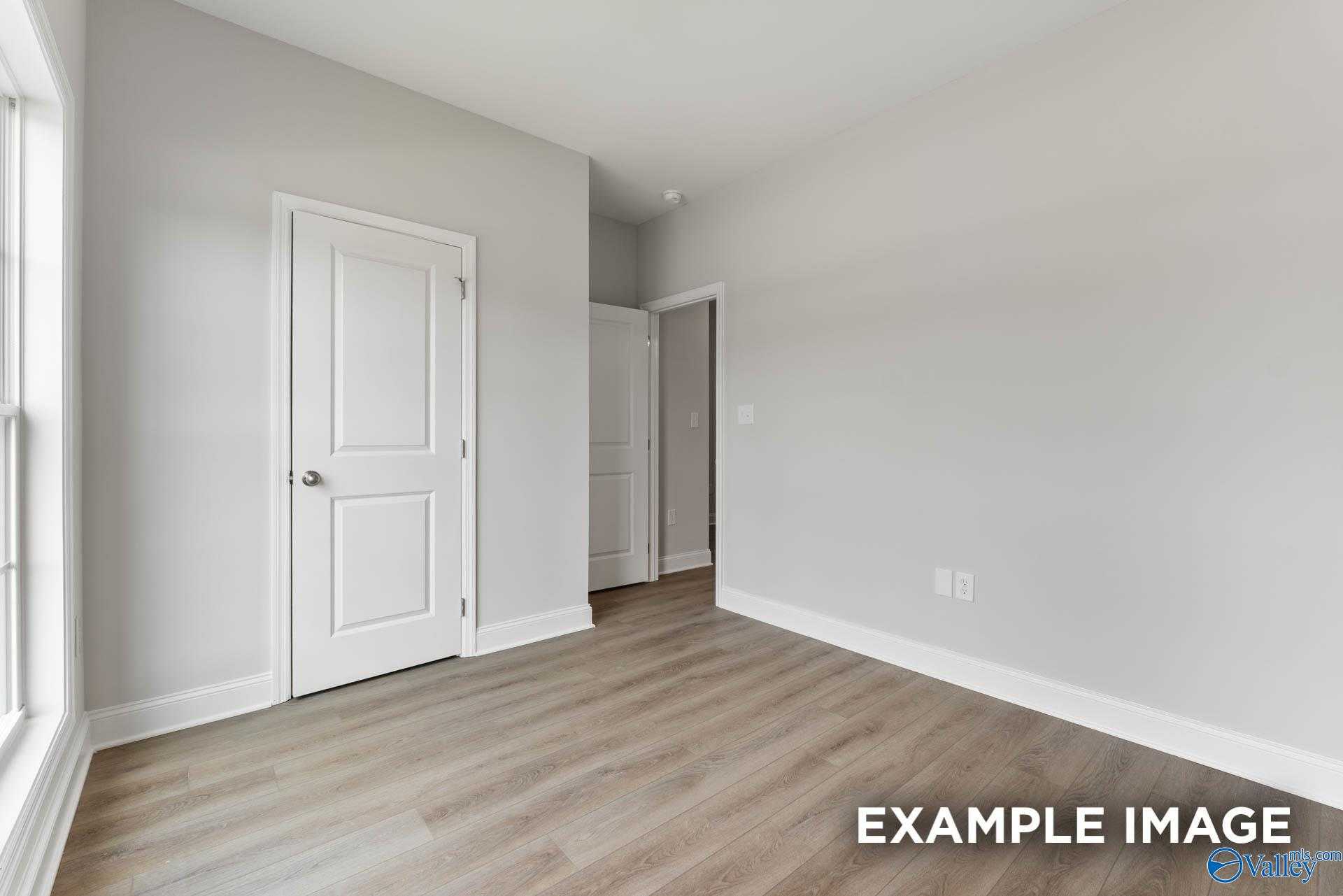 Bright empty bedroom with gray walls, white doors, laminate wood floors, and large window in Davidson Homes The Asheville C, Huntsville AL
