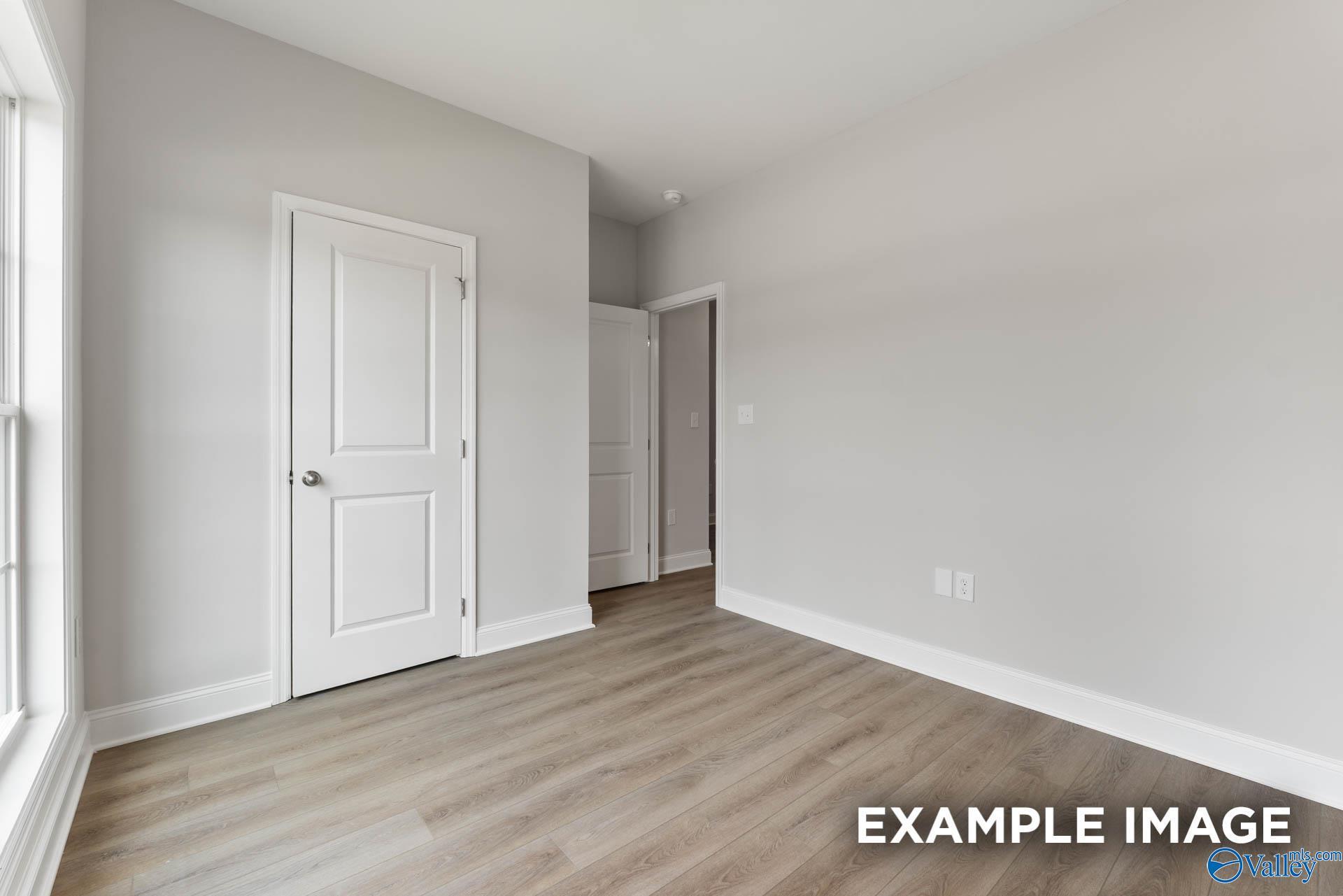 Spacious empty bedroom with gray walls, white doors, large window, and light hardwood floors in Davidson Homes The Asheville, Huntsville AL