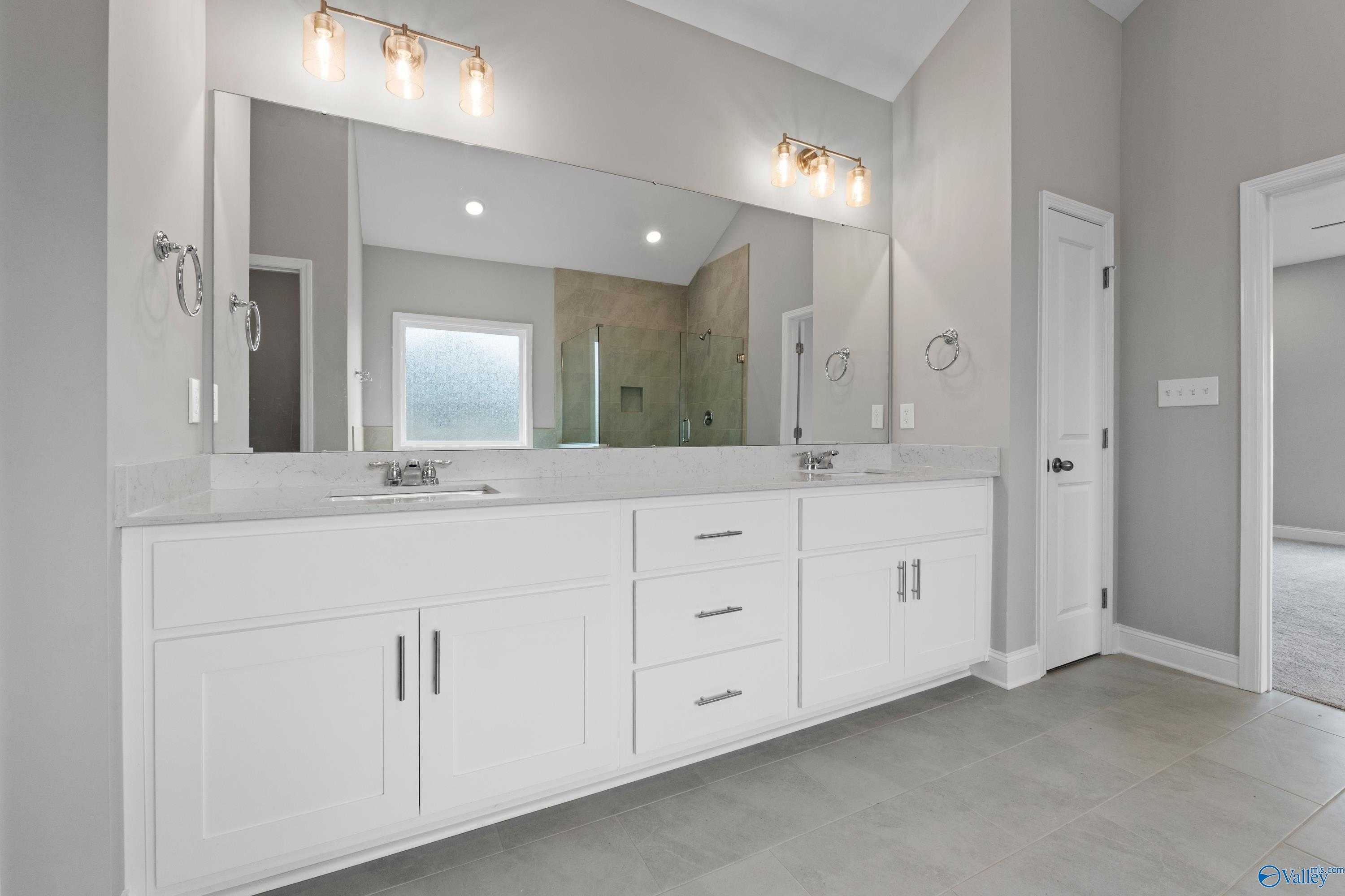 Modern master bathroom with double vanity, white cabinets, quartz counters, and glass shower in Davidson Homes The Finleigh, Meridianville, Alabama
