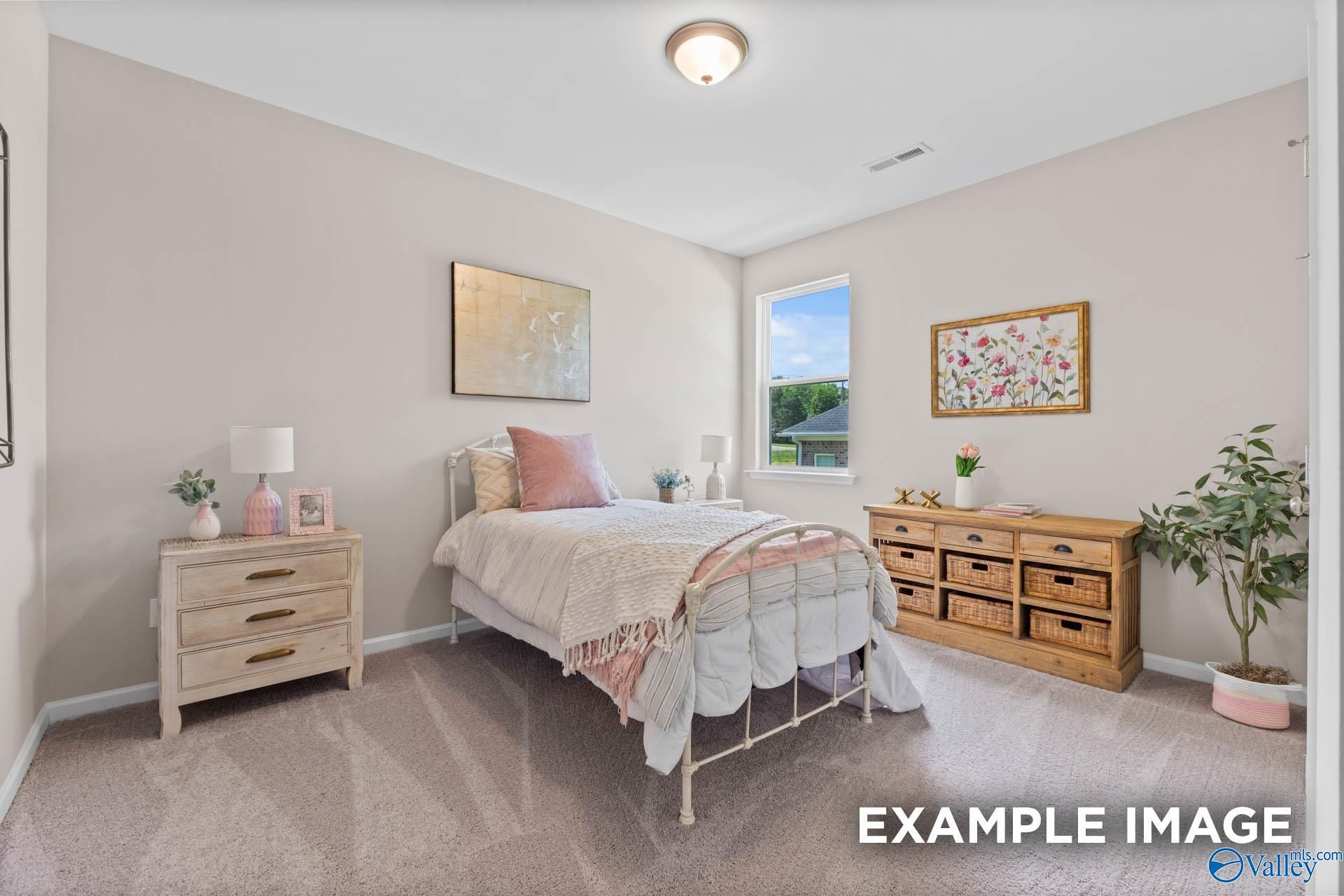 Cozy bedroom with pink bedding on metal frame bed, wooden nightstands, dresser, plants, and window in Evermore Homes The Arcadia M, Owens Cross Roads, Alabama