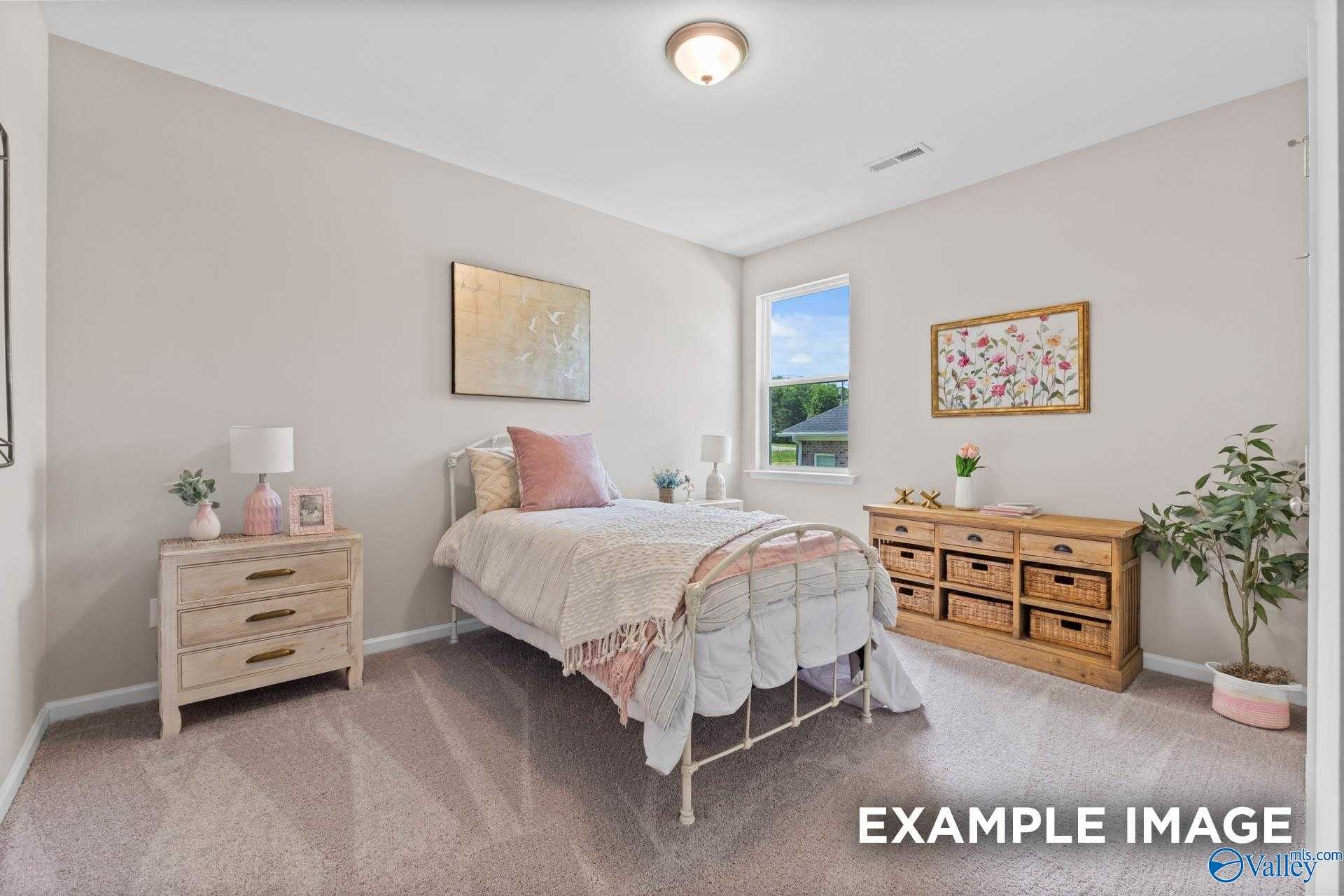 Cozy bedroom with pink bedding on metal frame bed, wooden nightstands, dresser, plants, and window in Evermore Homes The Arcadia M, Owens Cross Roads, Alabama