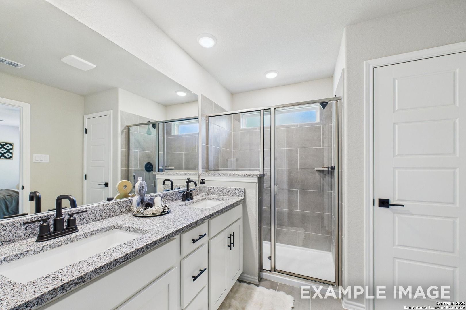 Modern master bathroom featuring double granite vanity, white cabinets, and frameless glass shower in Davidson Homes The Charlotte A, San Antonio