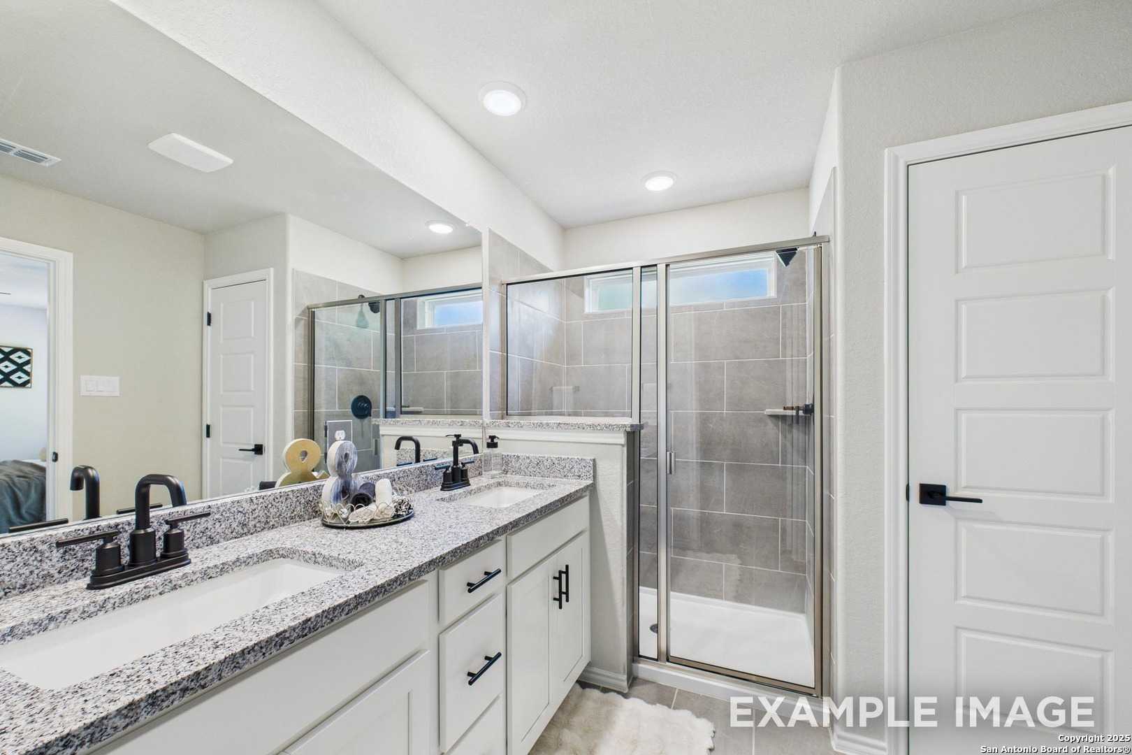 Modern master bathroom featuring double granite vanity, white cabinets, and frameless glass shower in Davidson Homes The Charlotte A, San Antonio