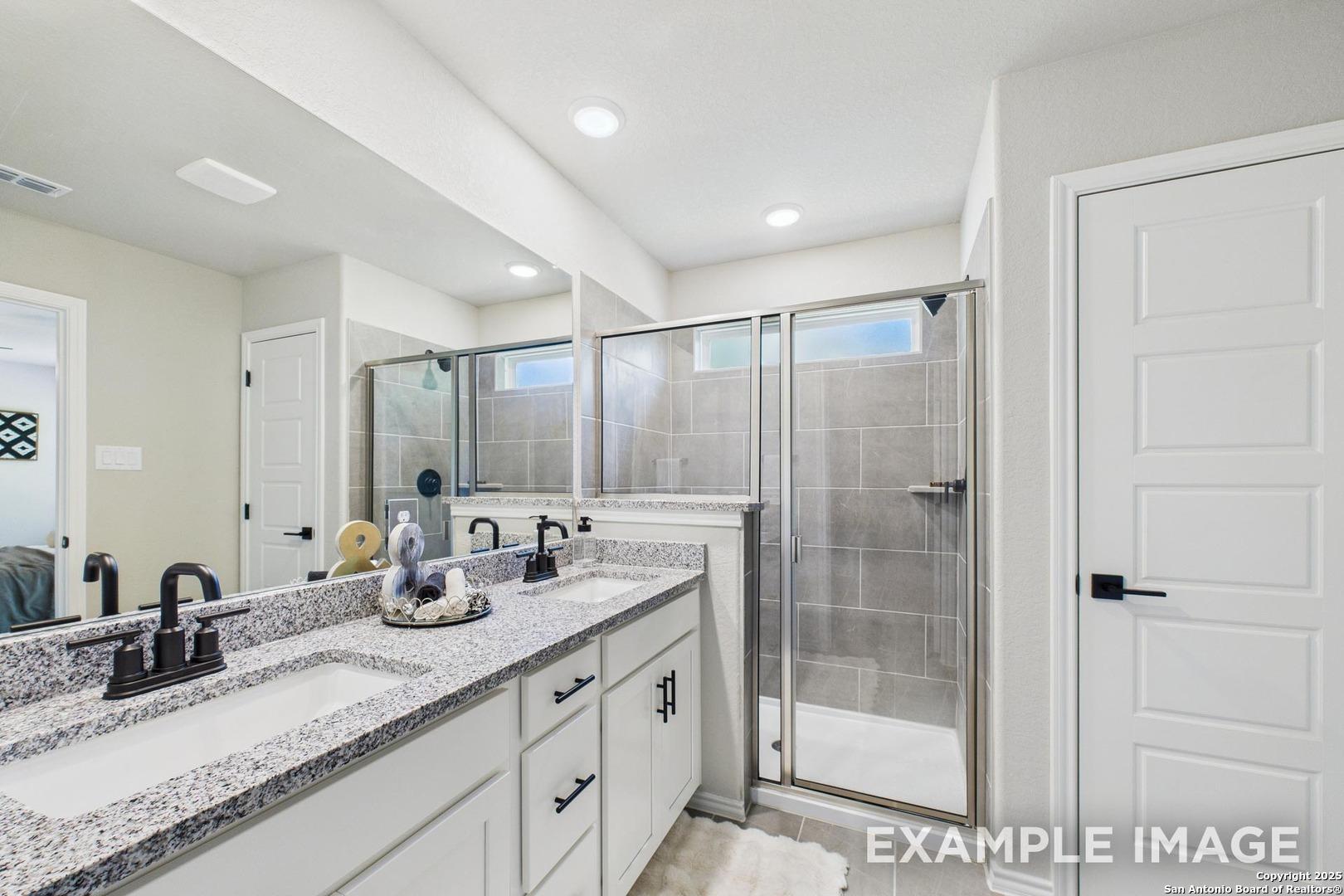 Elegant master bathroom with double granite vanity, frameless glass shower, and white cabinets in Davidson Homes The Charlotte B, San Antonio