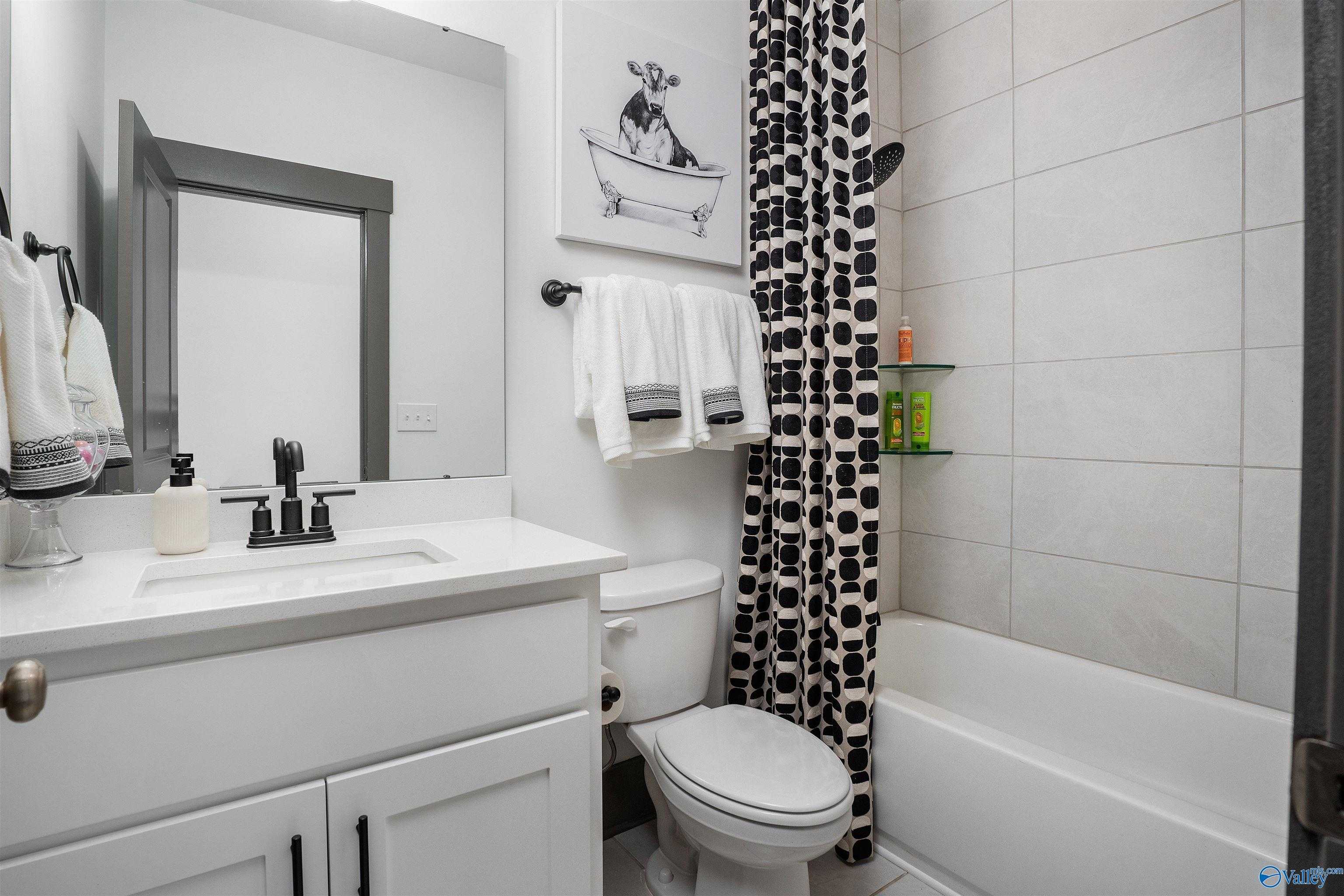 Modern guest bathroom featuring white vanity, cow shower curtain, subway tile, and black fixtures in Davidson Homes The Rockford B, Madison, AL