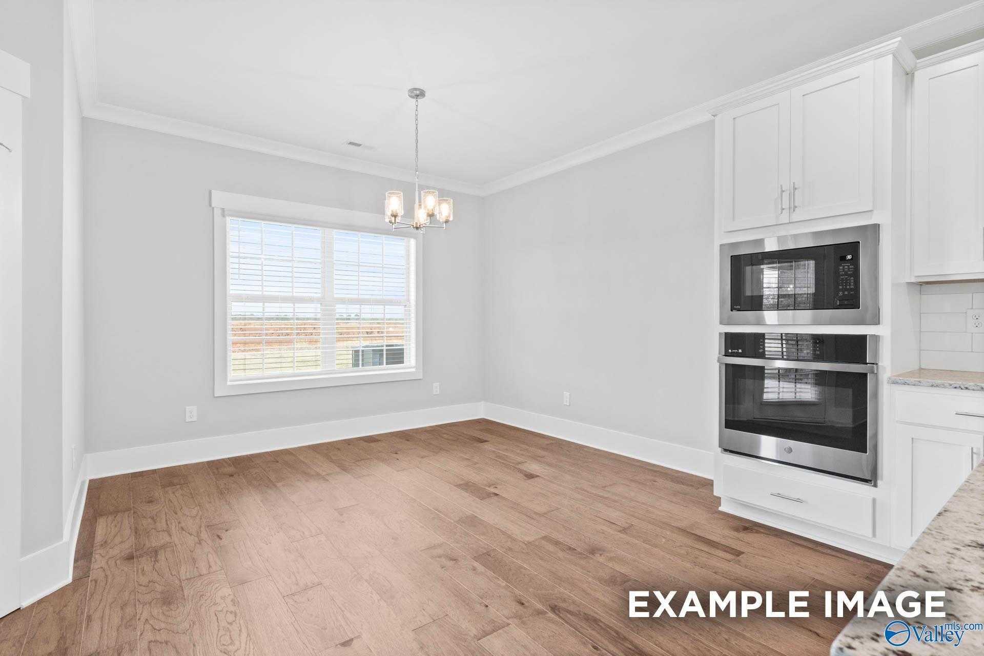Bright dining room with hardwood floors, large window, pendant light, and adjacent kitchen with white cabinets, double oven in The Rockford by Davidson Homes