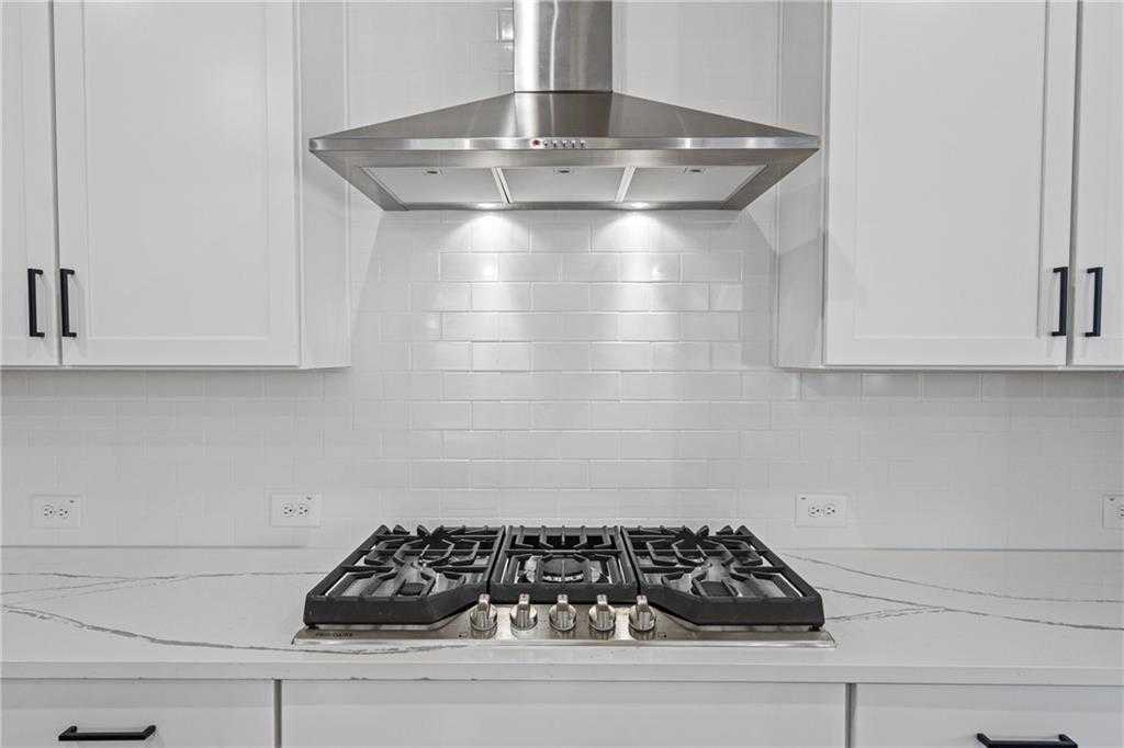 Modern kitchen featuring white shaker cabinets, stainless steel range hood, gas cooktop on quartz countertop in Davidson Homes The Edison A, Loganville, GA