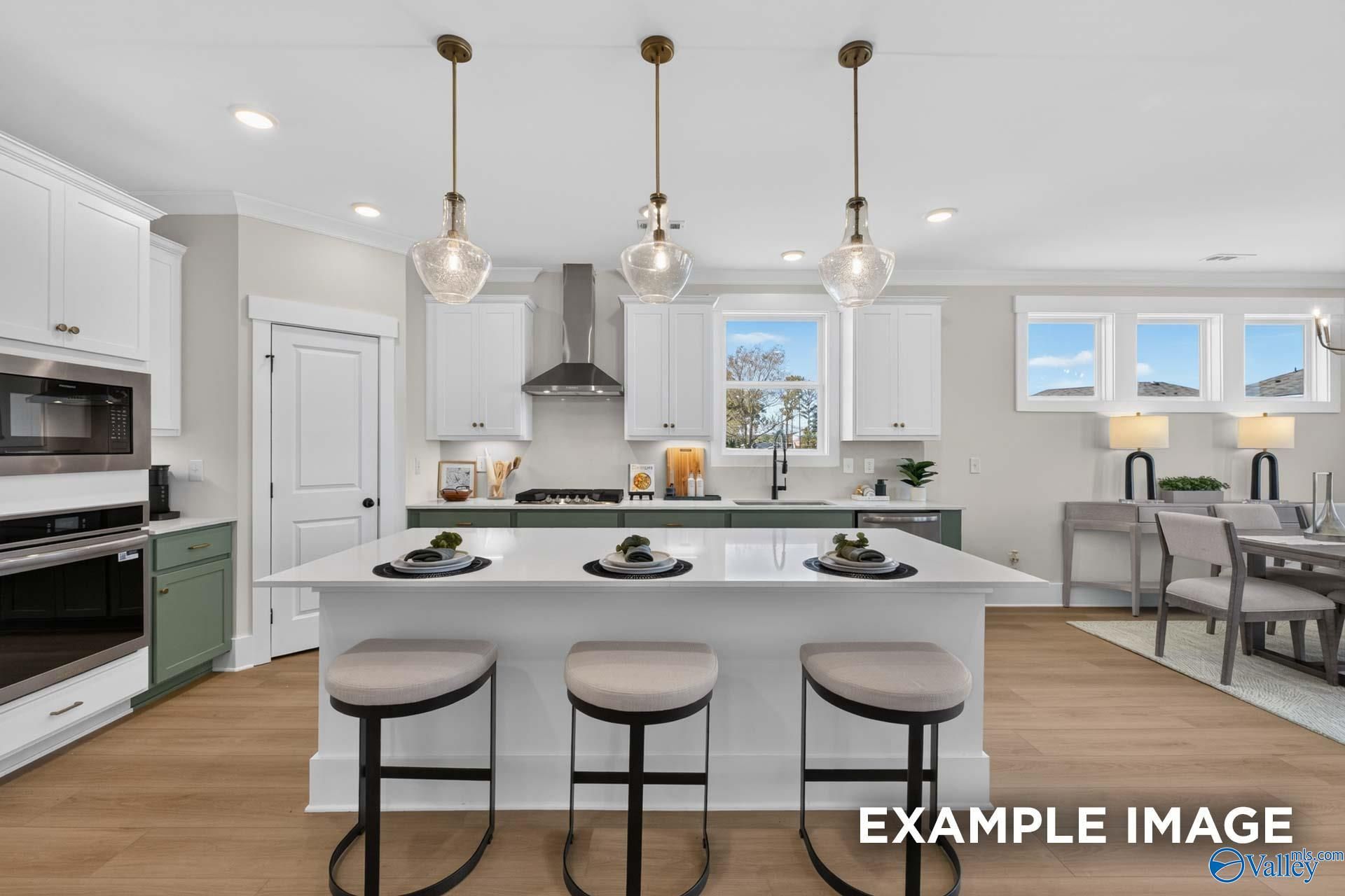 Open-concept kitchen with large island, green cabinets, and glass pendant lights in Davidson Homes The Ashport K, Hazel Green, Alabama