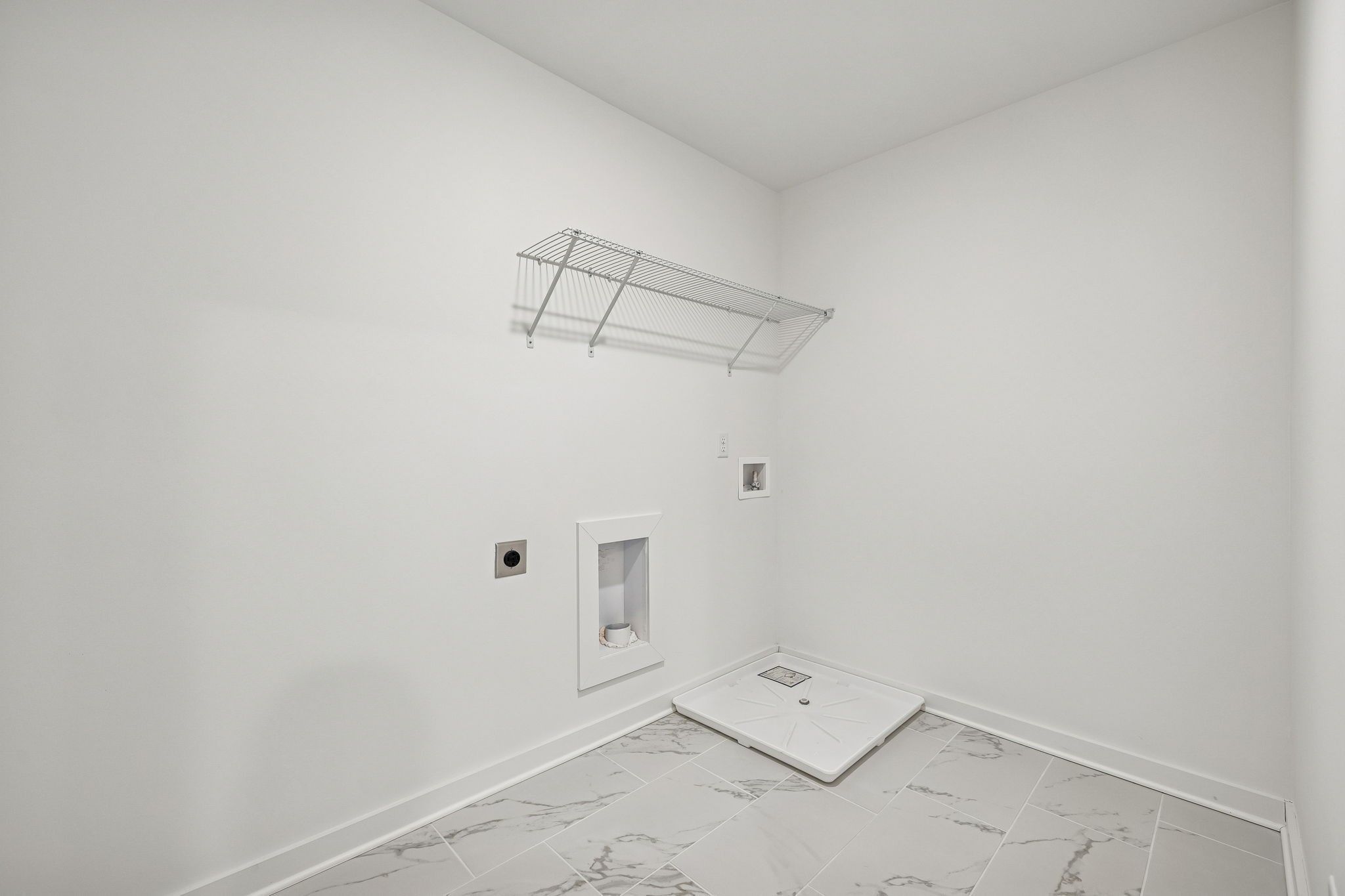 Modern laundry room with wire shelving, utility sink, washer hookups, and gray marble tile floor in Davidson Homes The Willow, Calista Farms