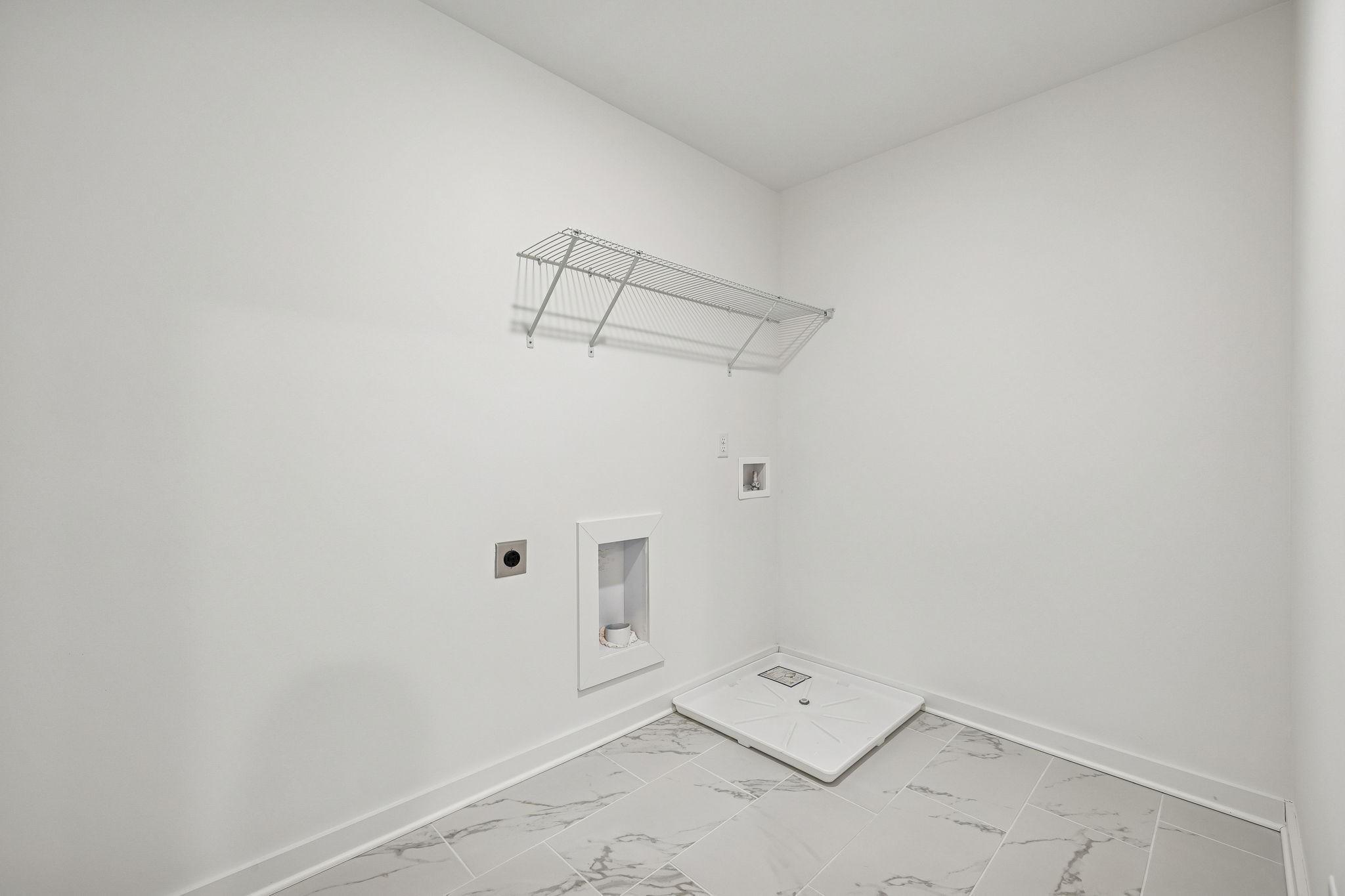 Modern laundry room with wire shelving, utility sink, washer hookups, and gray marble tile floor in Davidson Homes The Willow, Calista Farms