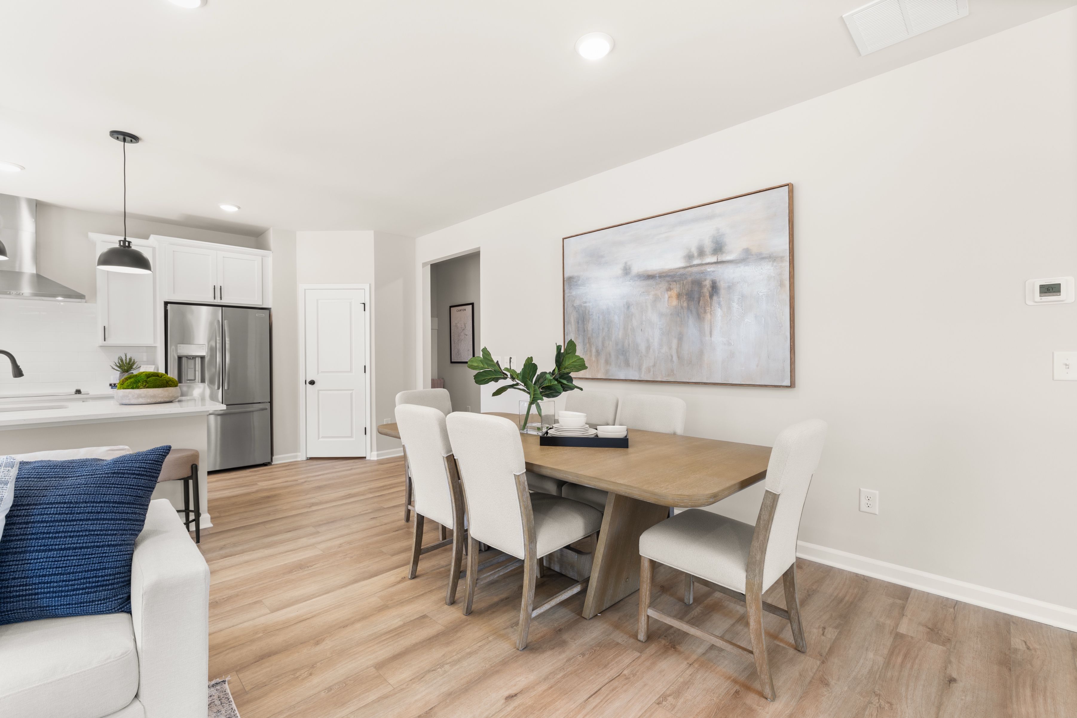 Elegant open-concept dining area at The Bluffs in Canton, Georgia by Davidson Homes with wood table, white chairs, abstract wall art, and modern kitchen
