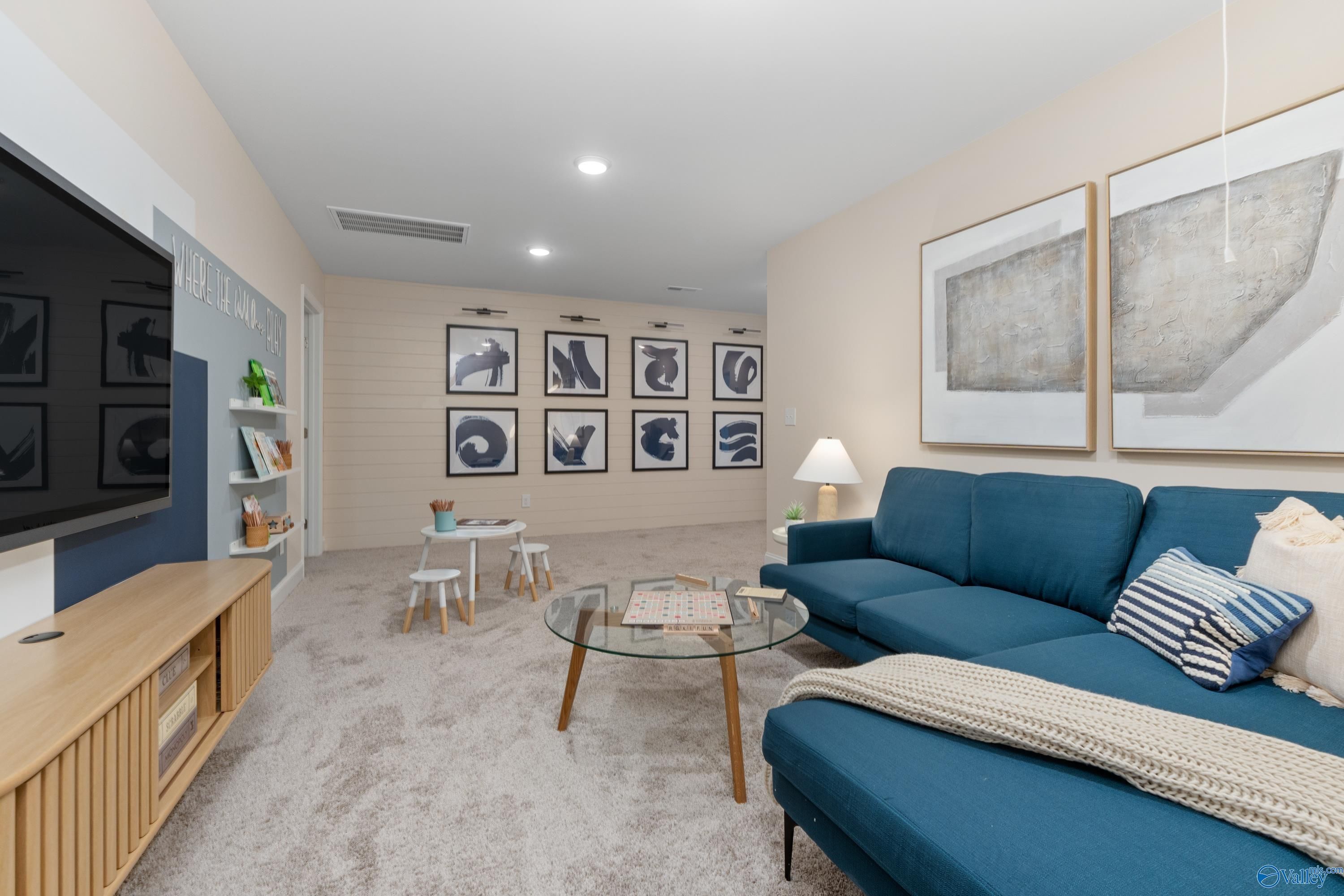 Cozy bonus room with blue sectional sofa, wall-mounted TV, abstract art, kids' table in Davidson Homes The Camden, Huntsville AL