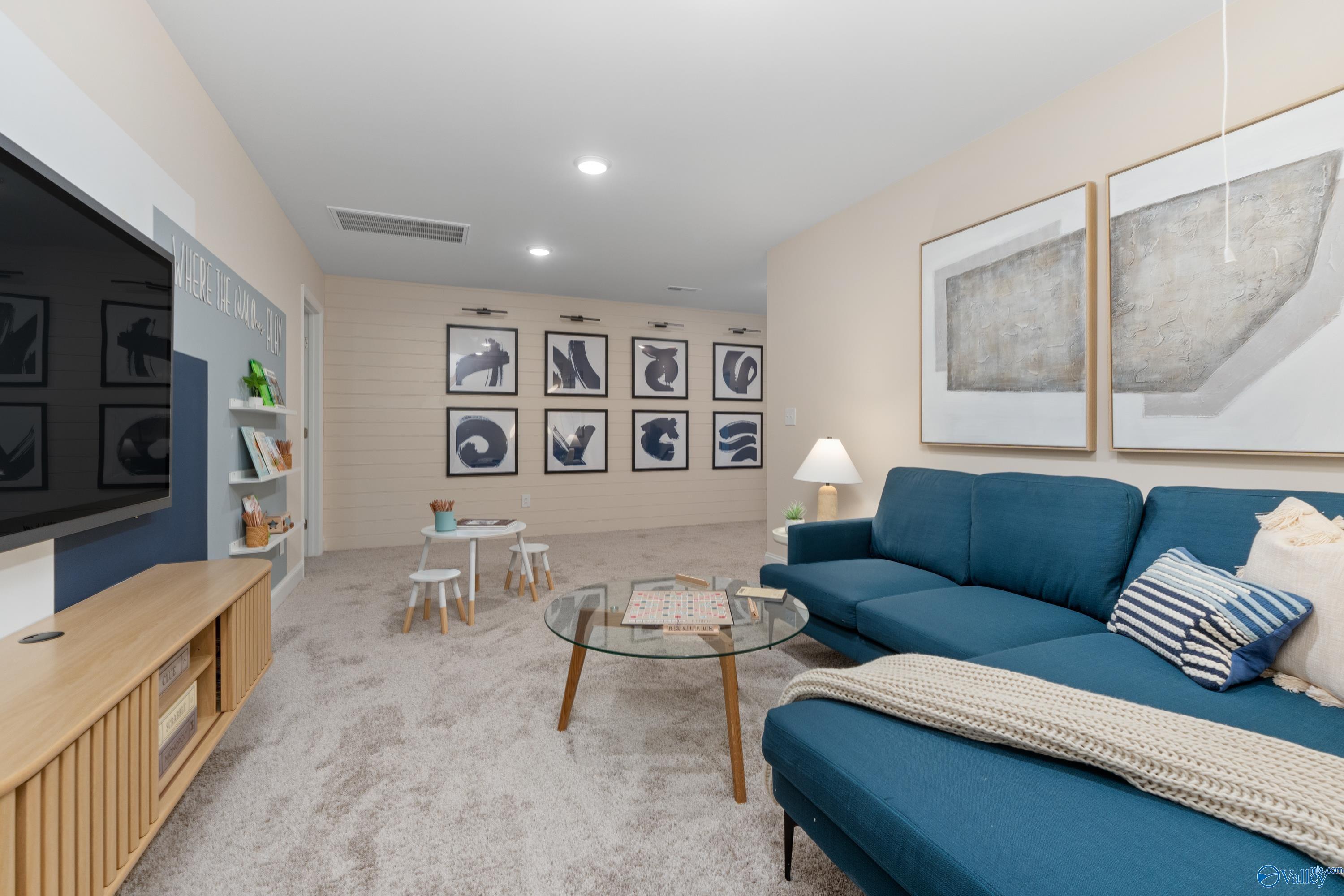 Cozy bonus room with blue sectional sofa, wall-mounted TV, abstract art, kids' table in Davidson Homes The Camden, Huntsville AL