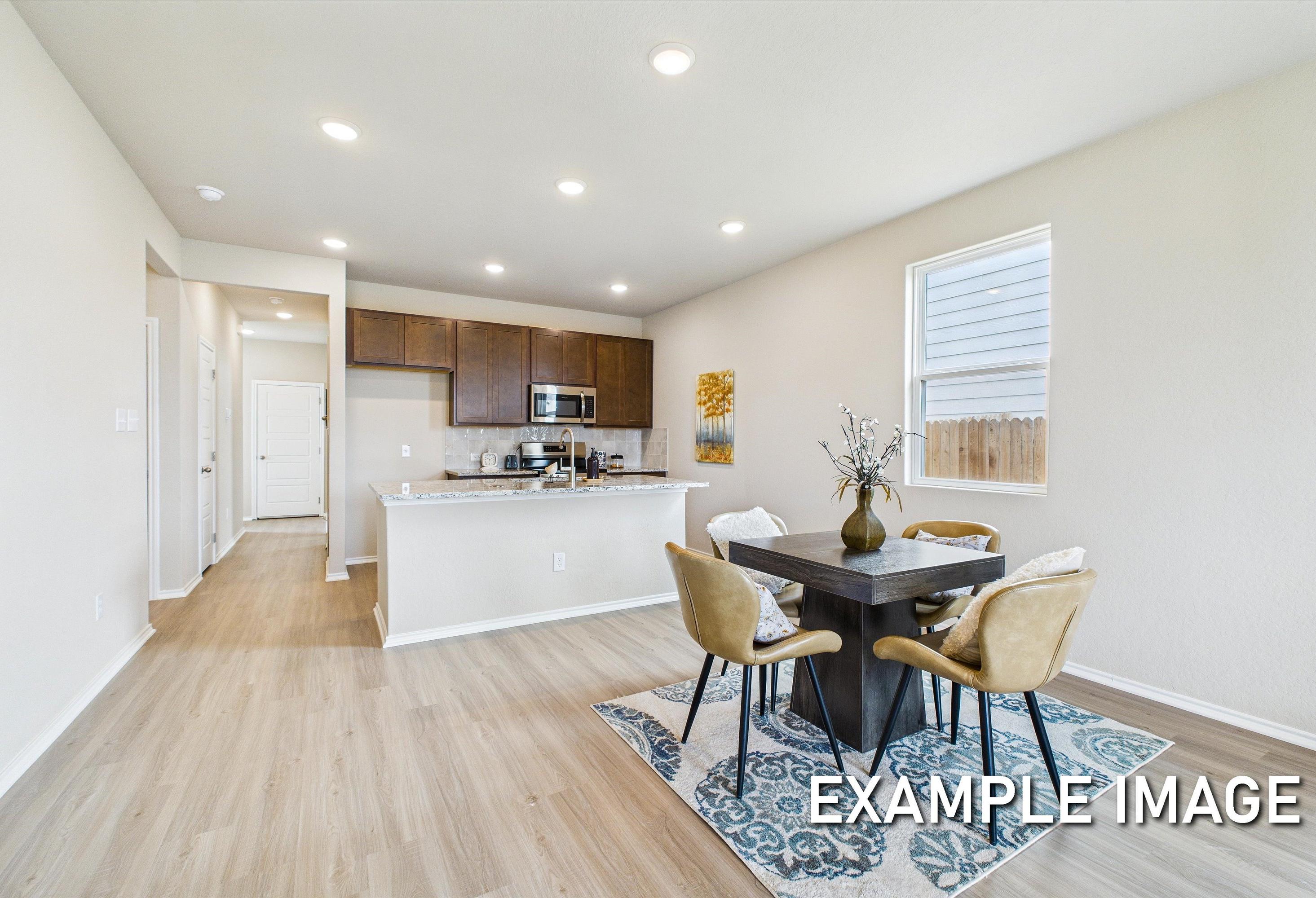 Open-concept kitchen and dining area in The Corral model home featuring modern cabinetry, granite counters, and wood floors.