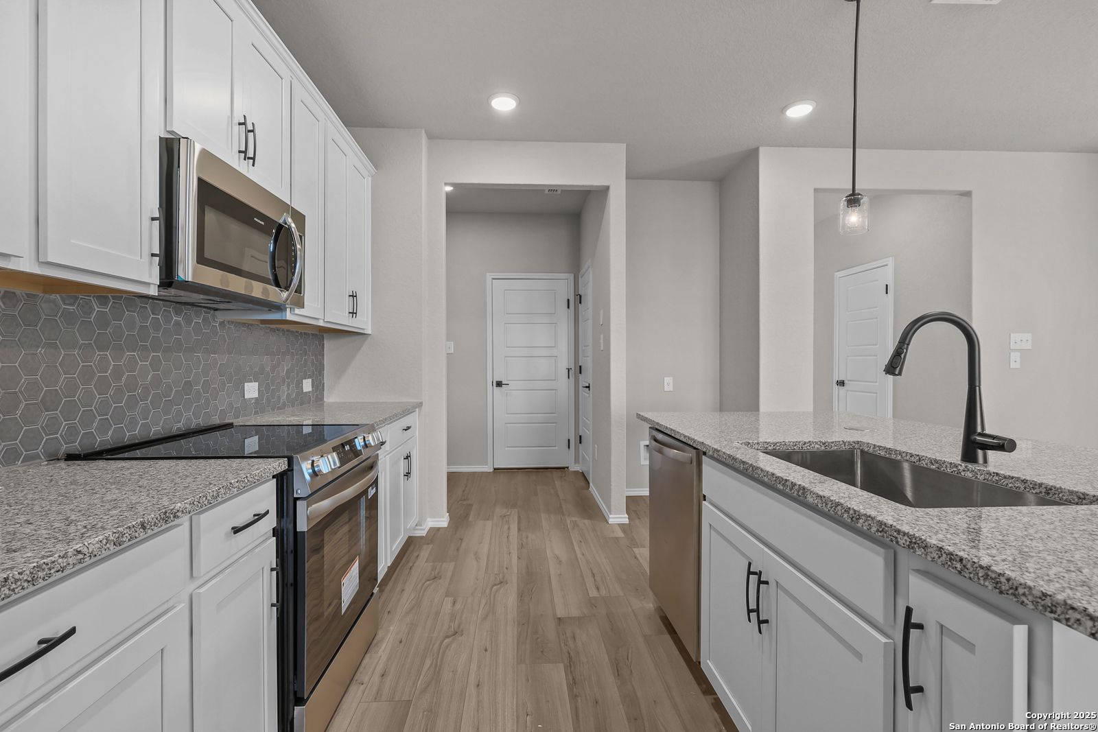 Modern open-concept kitchen with white cabinets, stainless appliances, granite island, hexagon backsplash in Davidson Homes The Brazos C, San Antonio