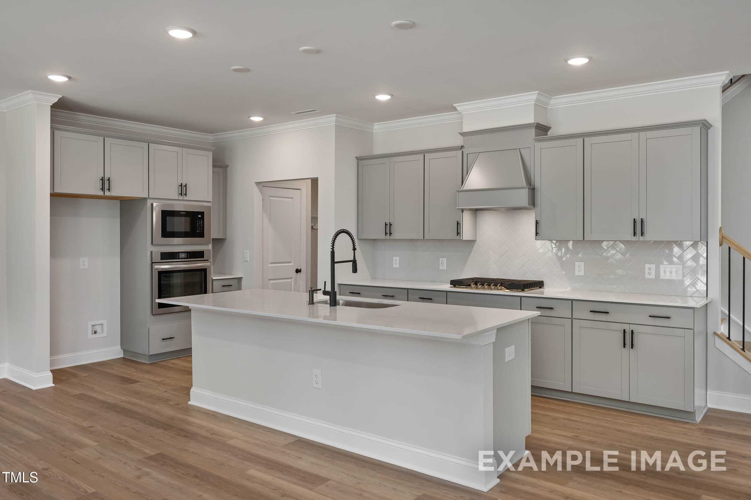 Elegant modern kitchen with gray shaker cabinets, white quartz island, stainless ovens and gas range in Davidson Homes The Beech B, Raleigh NC