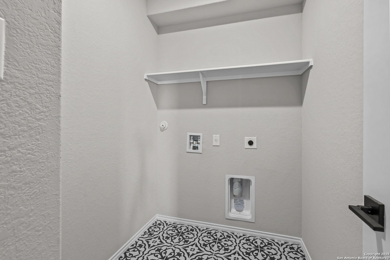 Modern laundry room with built-in white shelves, washer-dryer hookups, and patterned tile floor in Davidson Homes Daphne K, San Antonio
