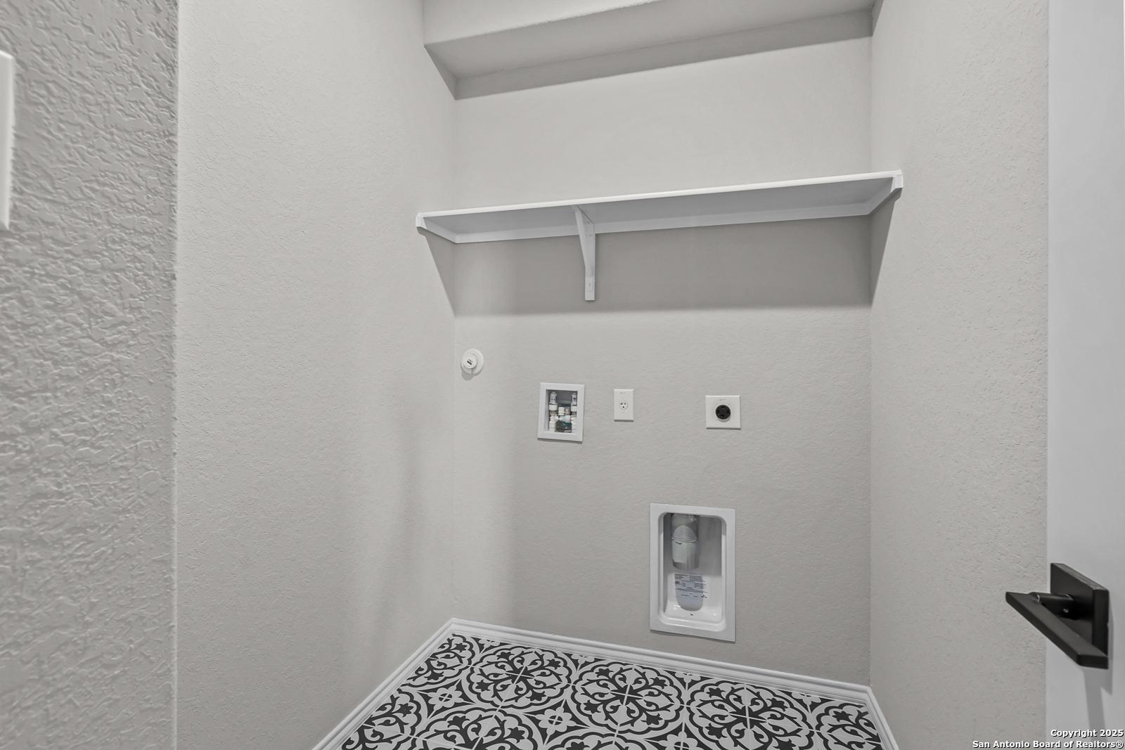 Modern laundry room with built-in white shelves, washer-dryer hookups, and patterned tile floor in Davidson Homes Daphne K, San Antonio