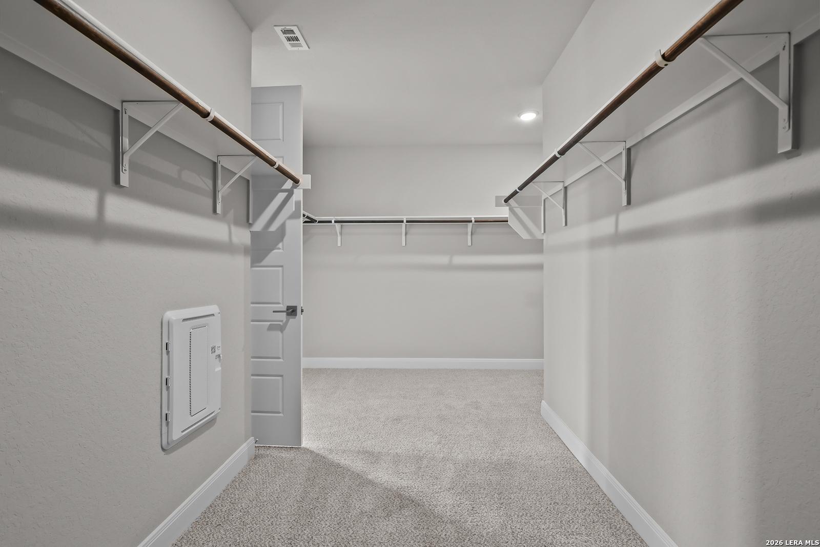 Spacious walk-in closet with wooden shelves and hanging rods in Davidson Homes The Rockford G, Ladera, San Antonio, Texas