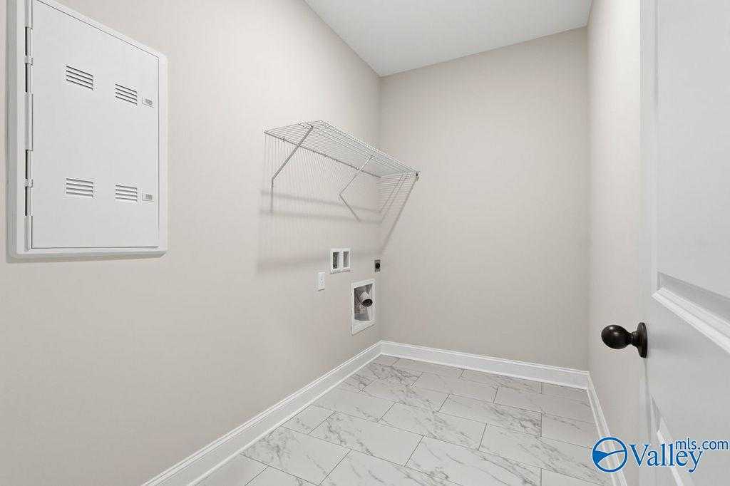 Modern laundry room with white louvered cabinet, glass shelf, washer hookups, and porcelain tile floor in The Rockford B home, Hartselle, AL
