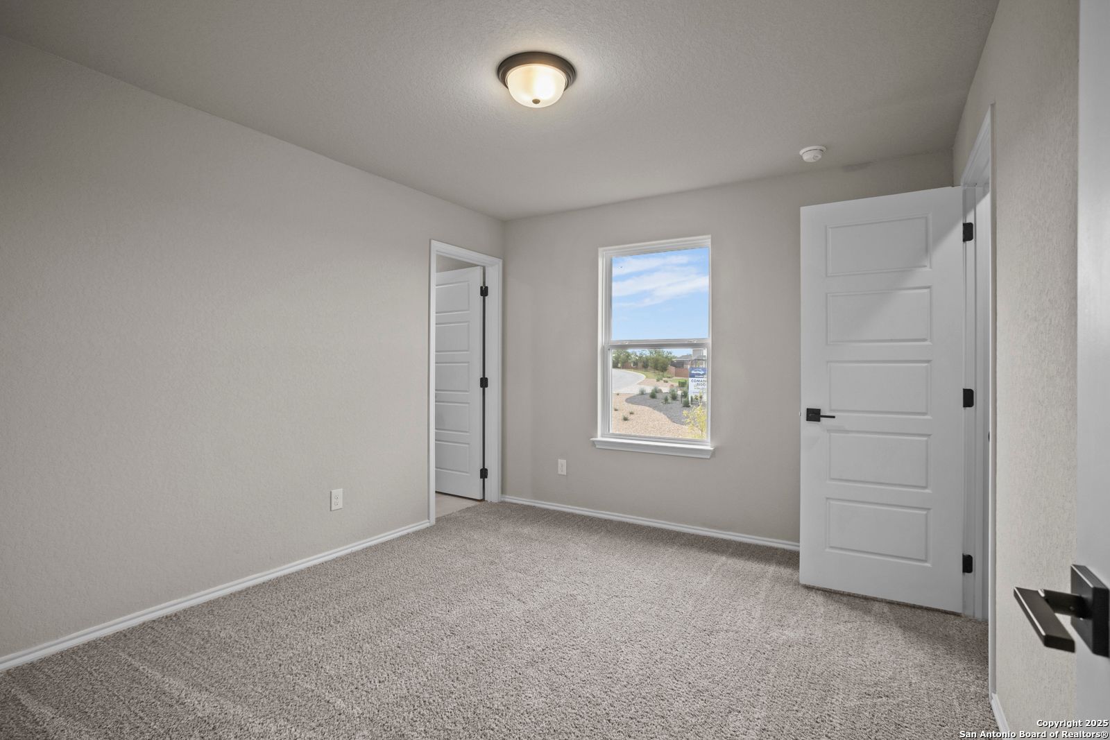 Bright secondary bedroom with light gray walls, neutral carpet, double doors, and scenic window view in Davidson Homes Douglas F, San Antonio