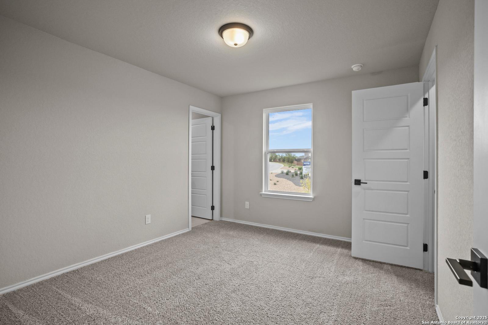 Bright secondary bedroom with light gray walls, neutral carpet, double doors, and scenic window view in Davidson Homes Douglas F, San Antonio