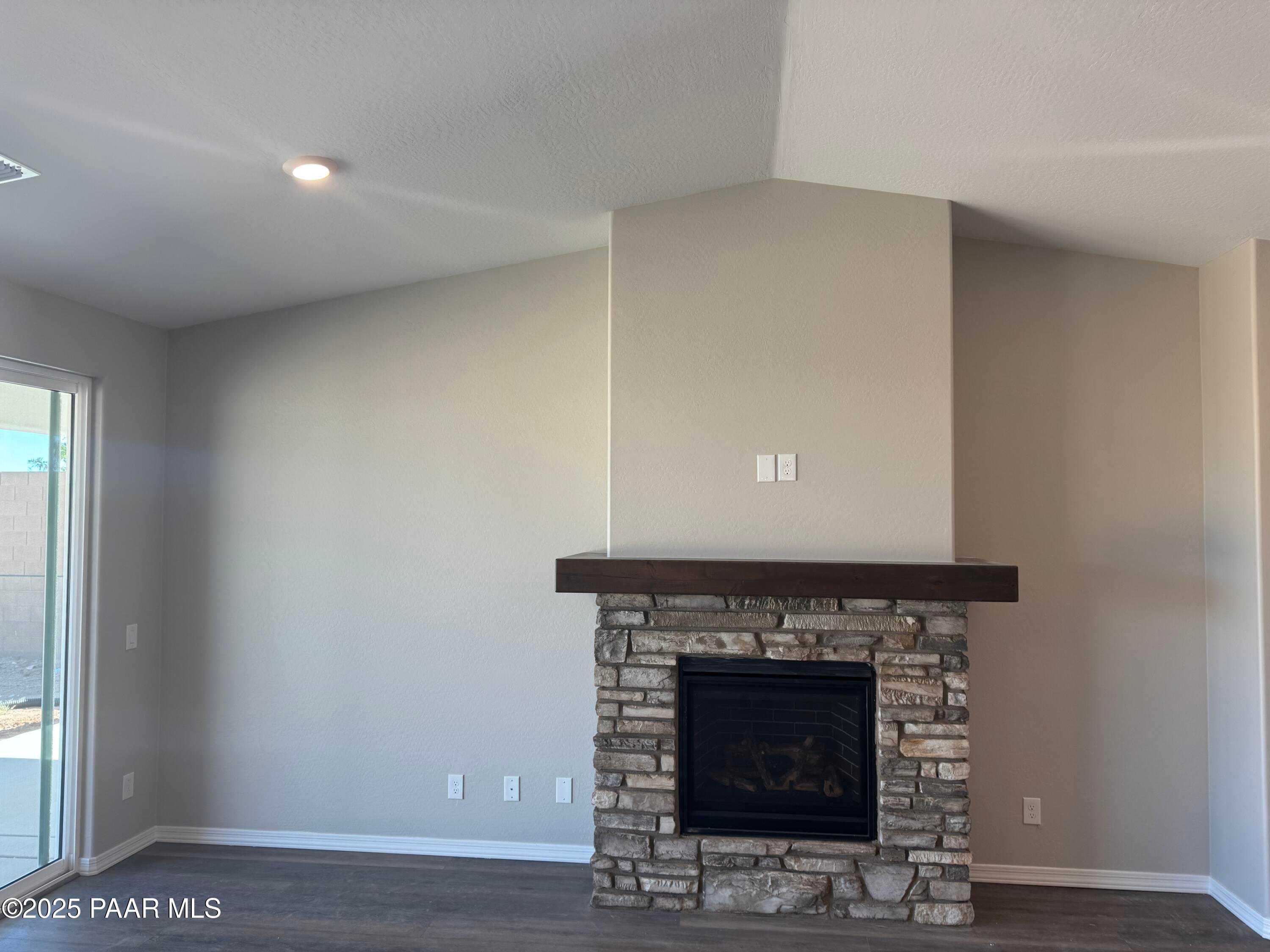 Cozy stone gas fireplace with wooden mantel and vaulted ceiling in living room of Davidson Homes The Monarch E, Prescott, Arizona