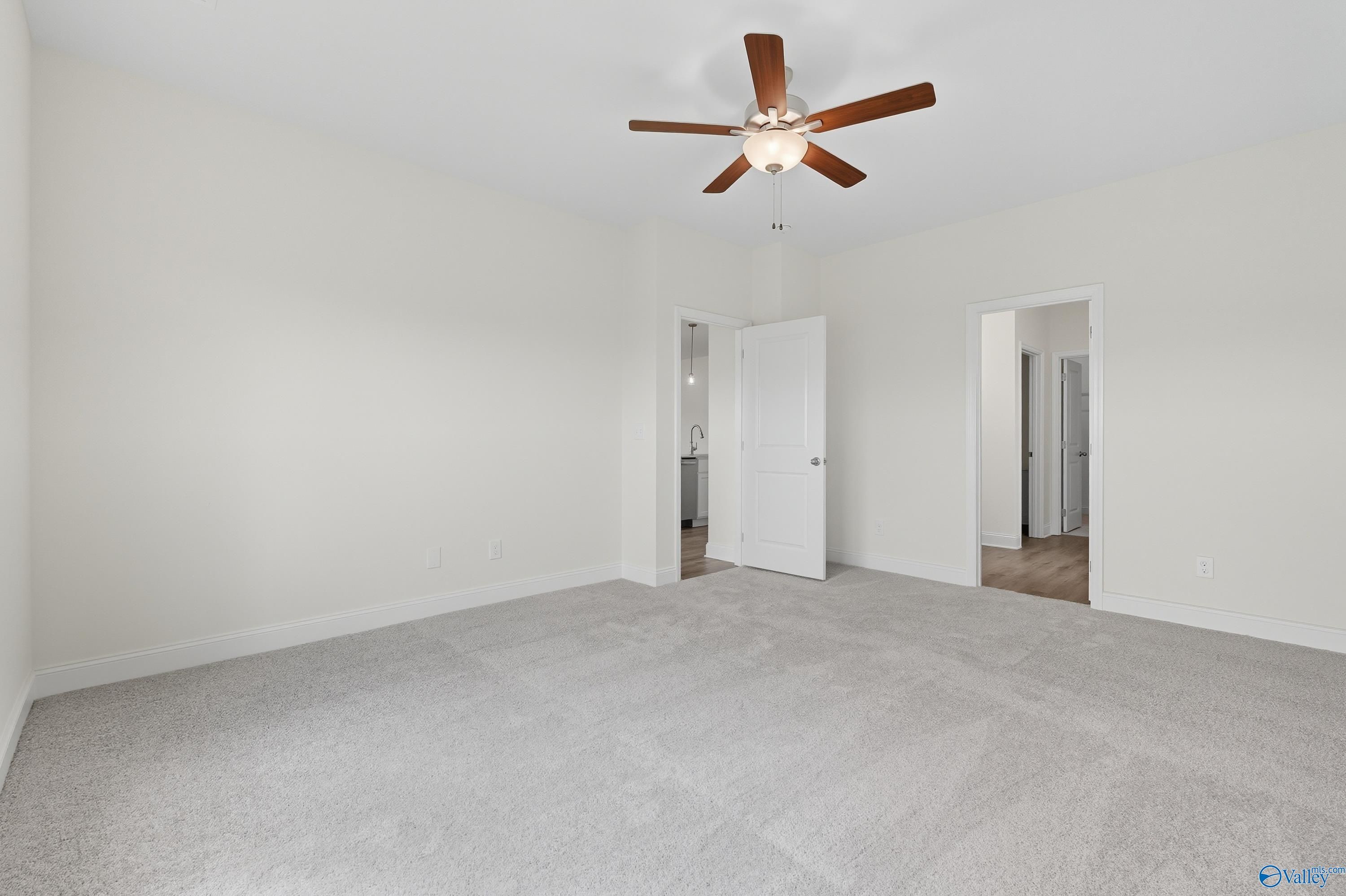 Spacious bedroom with ceiling fan, gray carpet, and open bathroom doorway in Davidson Homes The Everett, Meridianville, AL