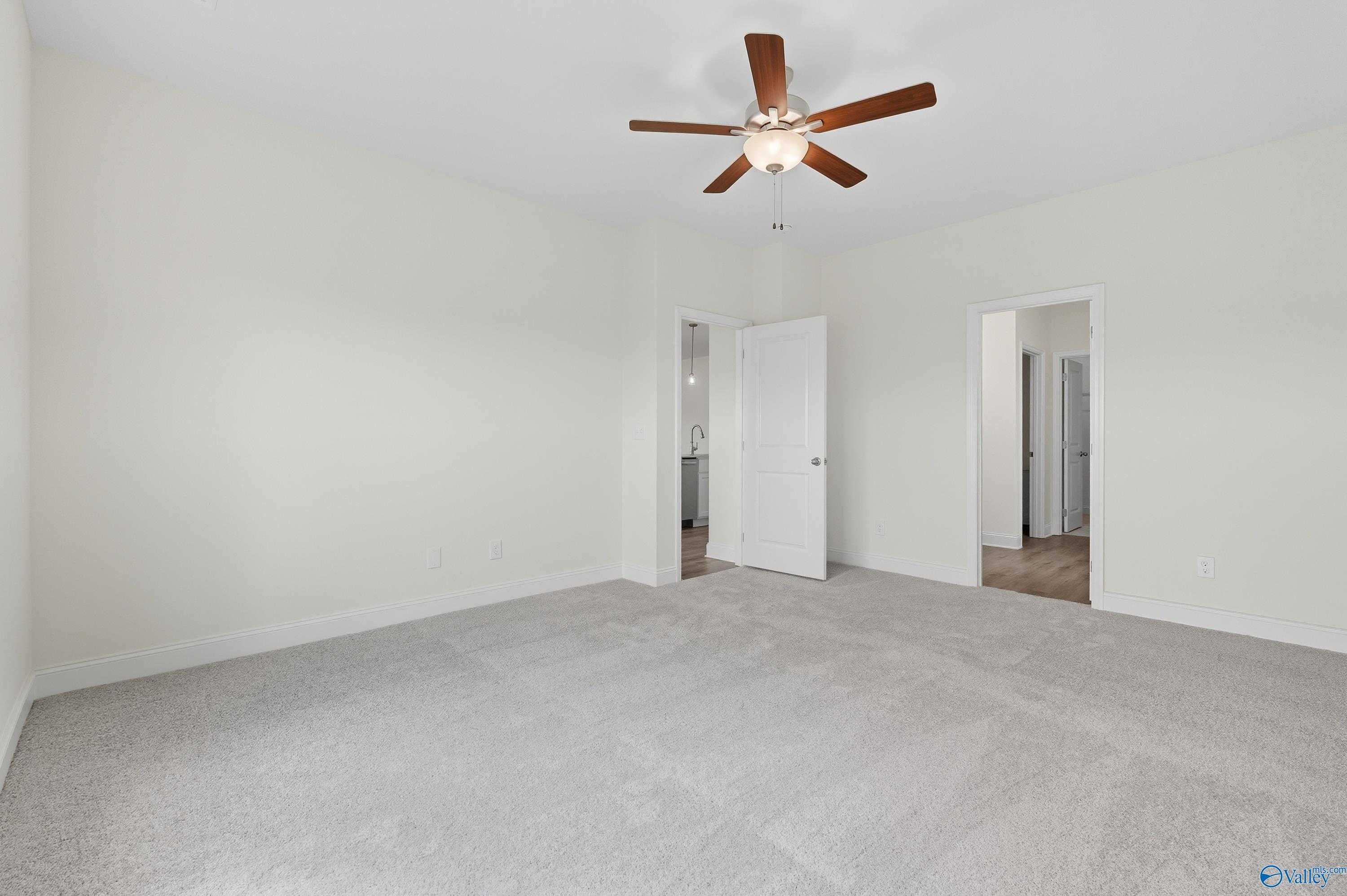 Bright bedroom with ceiling fan, white walls, gray carpet, and open doors to bath in Davidson Homes The Everett, Meridianville, AL