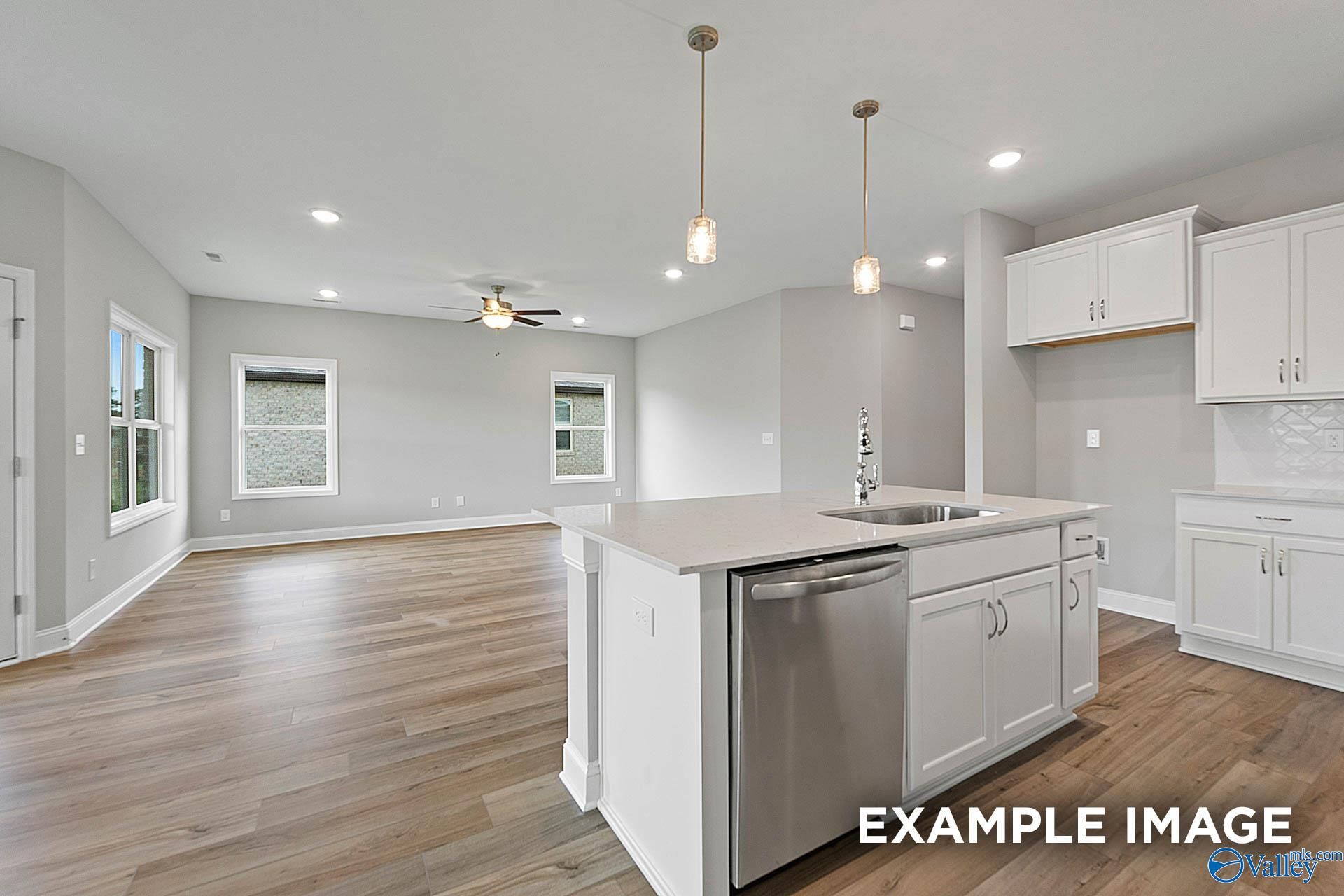 Open-concept kitchen with white cabinets, stainless dishwasher, large island and pendant lights in The Franklin E, Hazel Green, Alabama