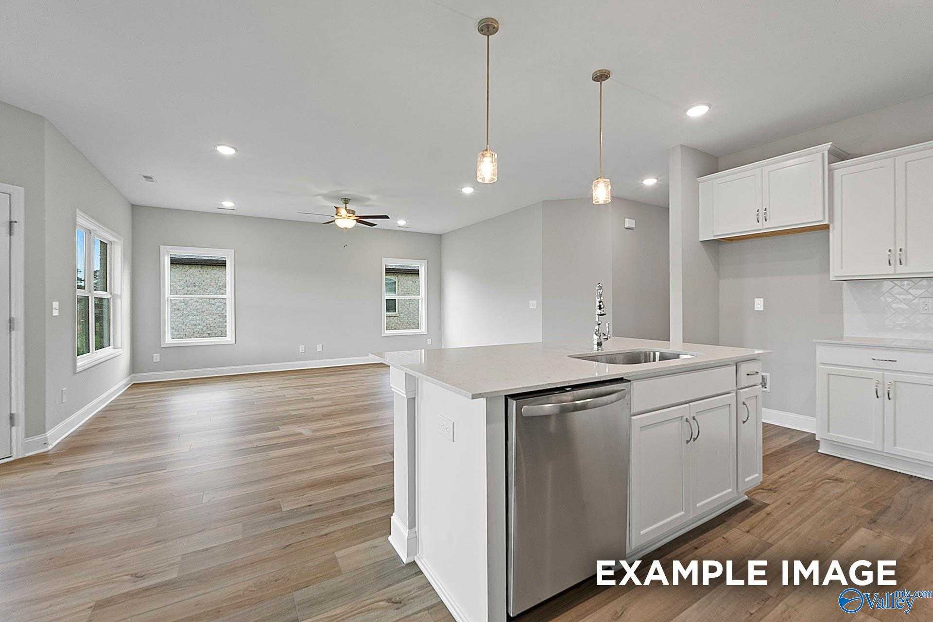 Open-concept kitchen with white cabinets, stainless dishwasher, large island and pendant lights in The Franklin E, Hazel Green, Alabama