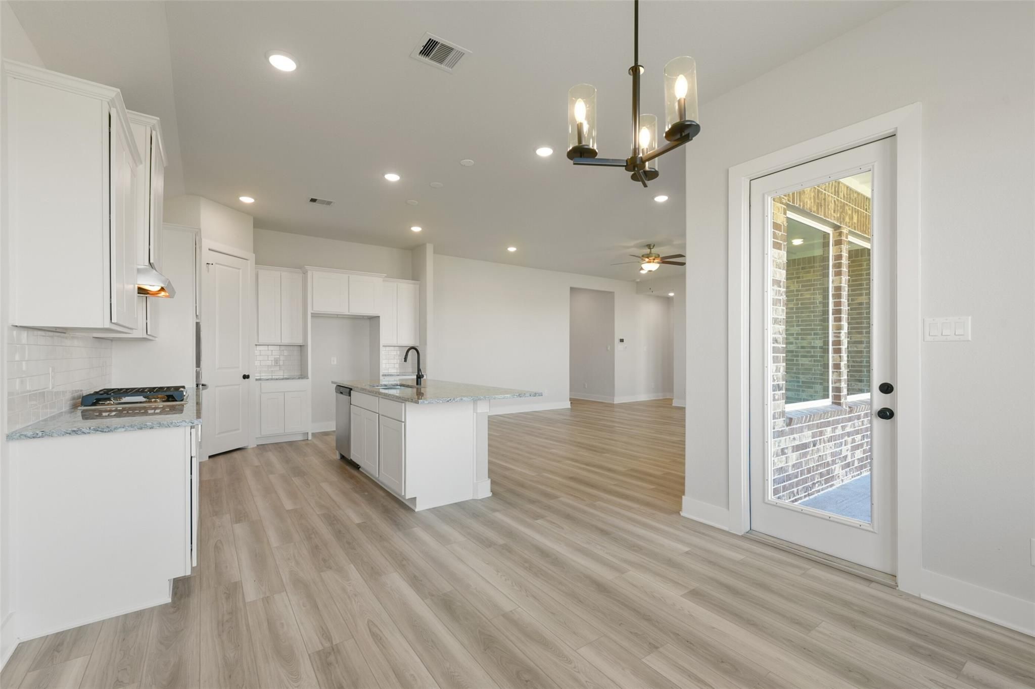 Modern open-concept kitchen with white cabinets, large island sink, and chandelier in Davidson Homes The Edward C, Lago Mar