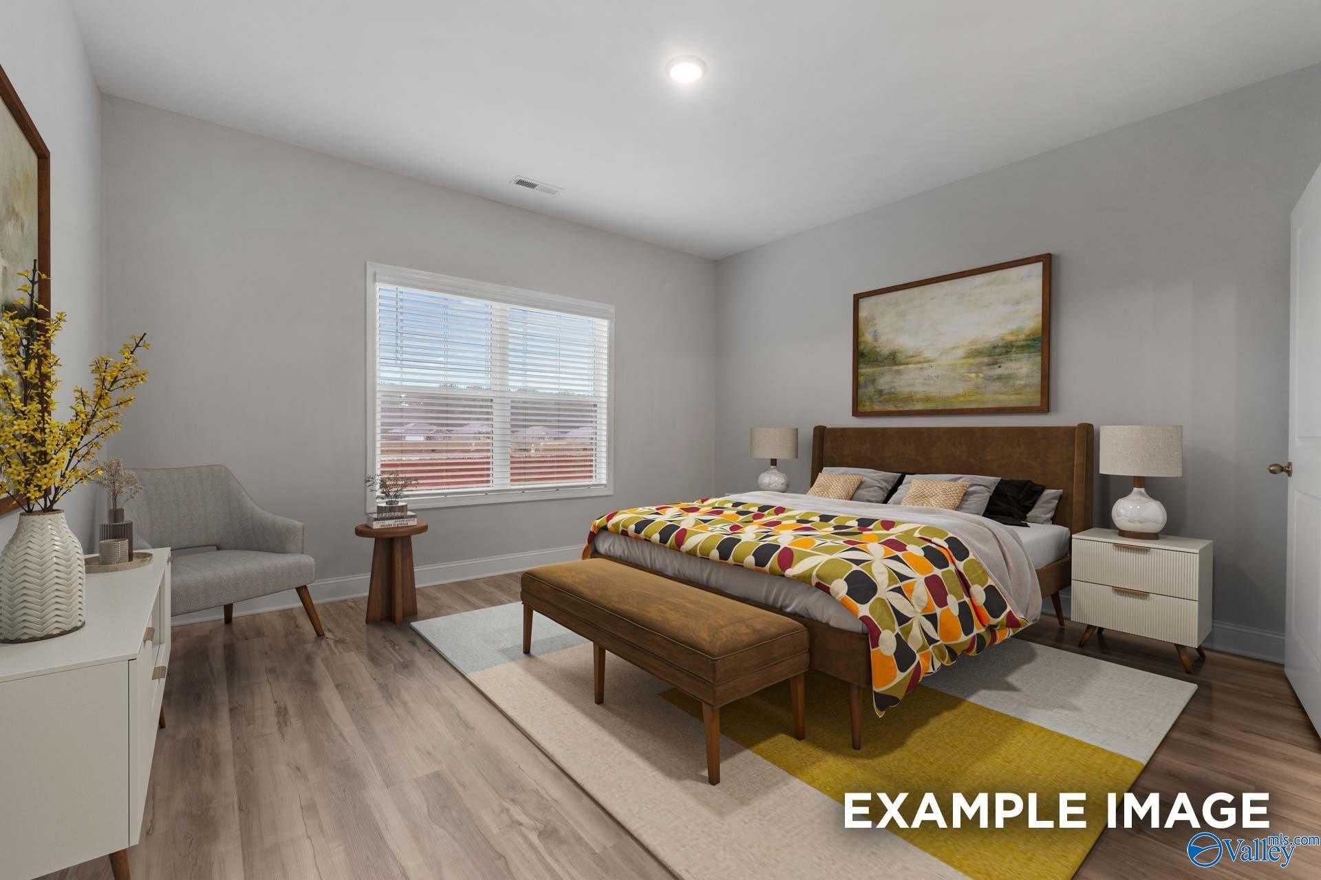 Cozy secondary bedroom with colorful king bed, gray walls, armchair, and wood floors in Davidson Homes The Cumberland B, Decatur, Alabama