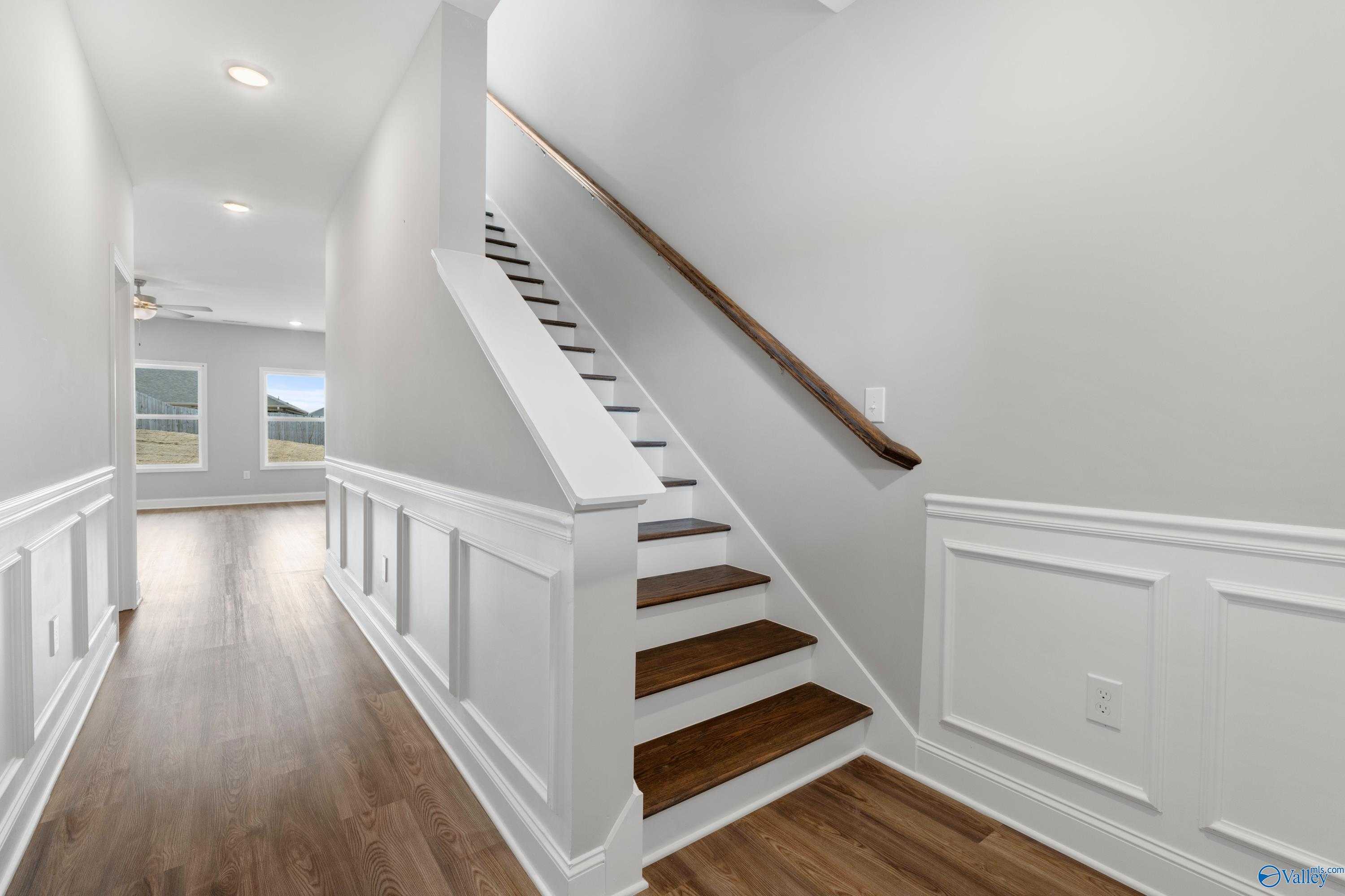 Elegant hallway with white wainscoting, hardwood floors, and wooden staircase in Davidson Homes The Aiken, Meridianville, Alabama