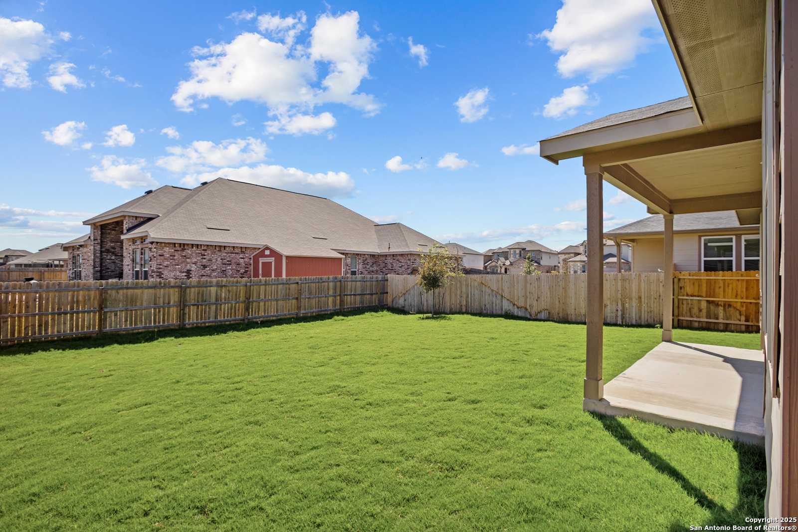 Private backyard with lush green lawn, wooden fence, and covered patio in Davidson Homes The Asheville E, Horizon Pointe, Converse, Texas