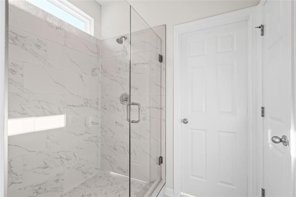 Modern white marble shower with frameless glass enclosure in master bath of Davidson Homes The Glenwood C, Hoschton, GA