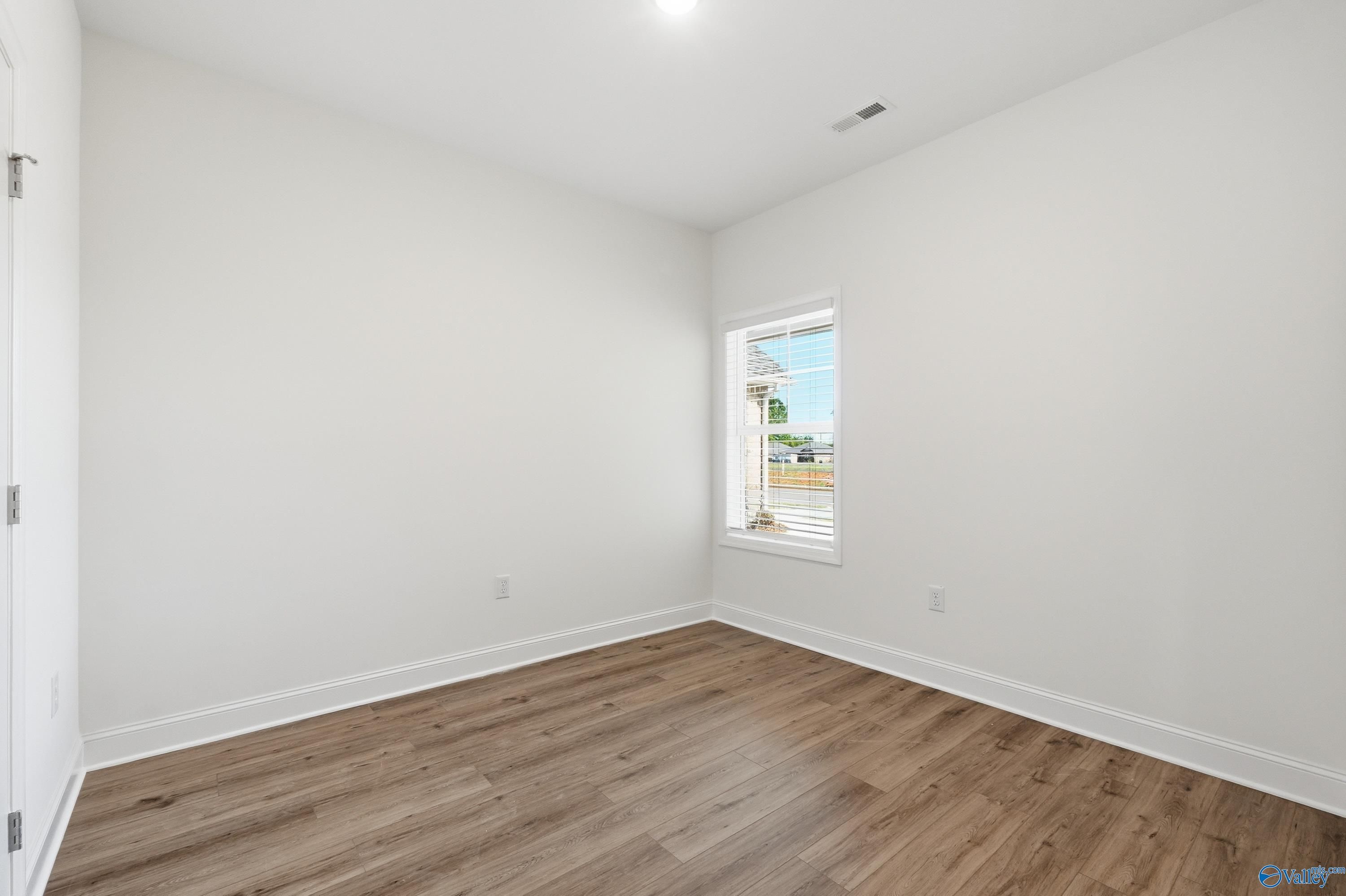 Bright empty bedroom with white walls, hardwood floors, and window overlooking greenery in Davidson Homes The Cumberland D, Decatur, AL