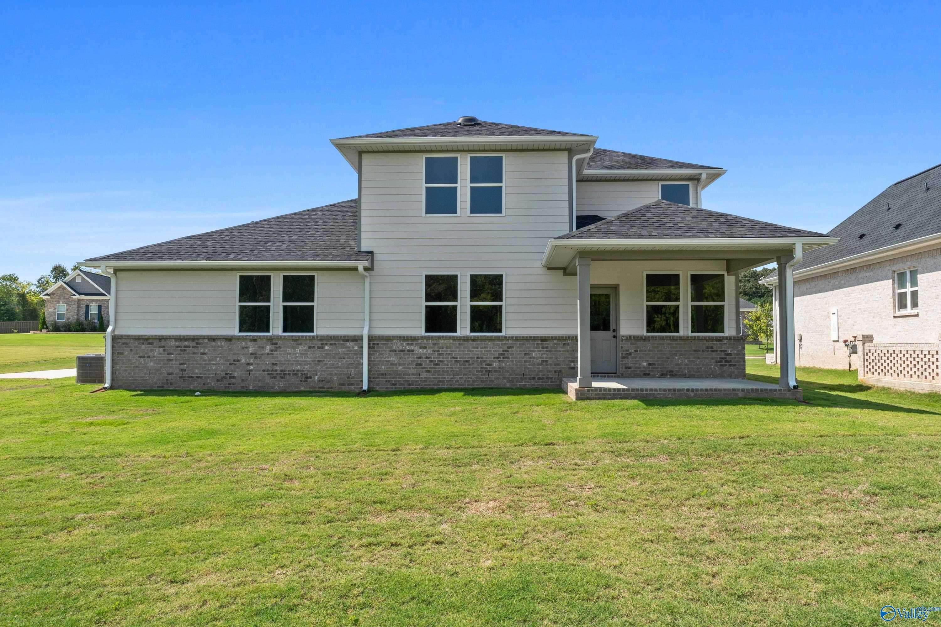 Rear view of two-story Dorado home featuring covered patio, brick accents, and lush green yard in Riverton Preserve, Huntsville, Alabama