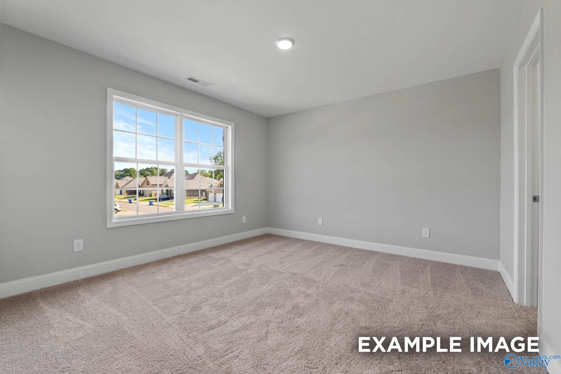 Bright empty bedroom with gray walls, beige carpet, and large window view of suburban neighborhood in The Shelby B, New Market, AL