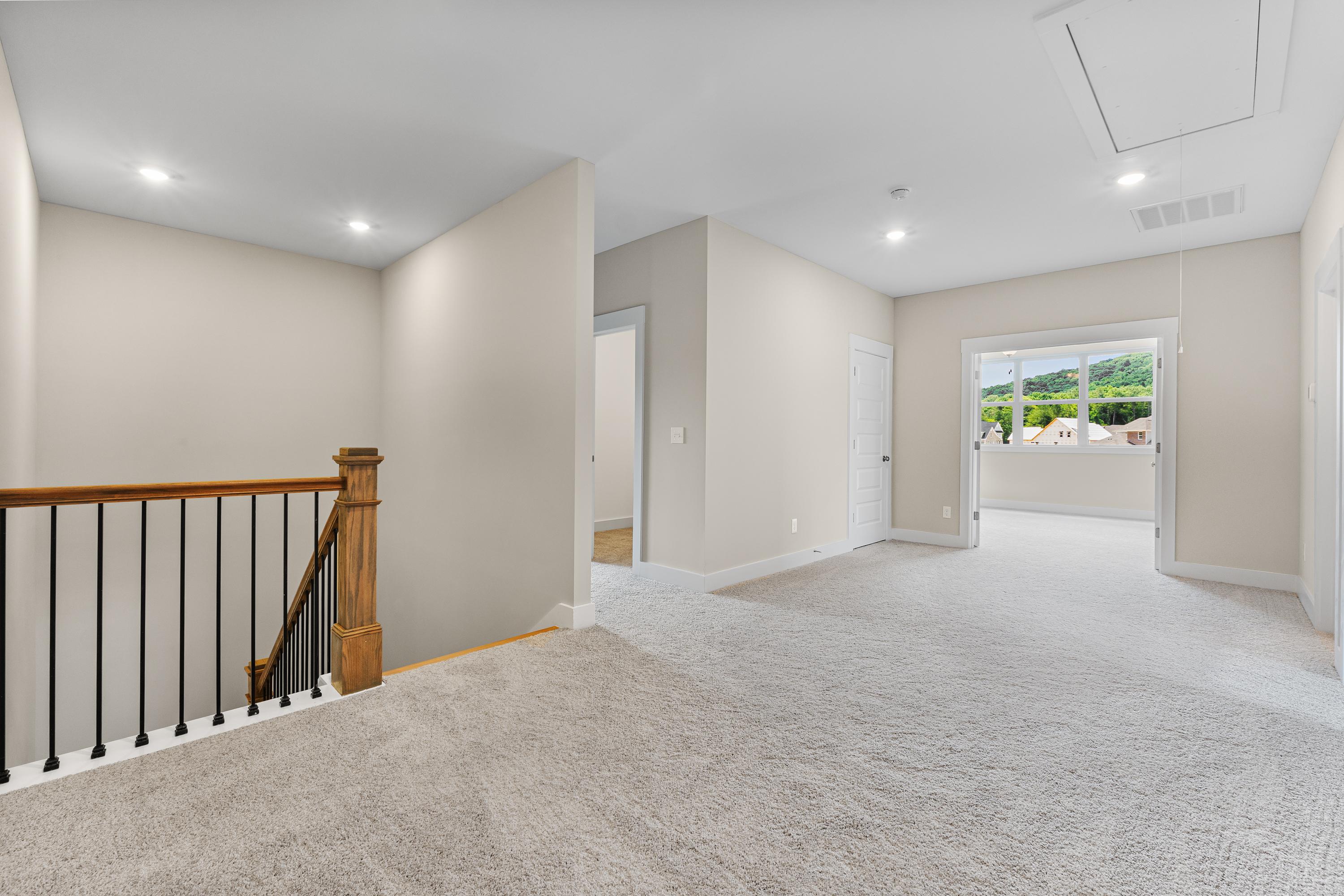 Upper level hallway in The Oxford A showcasing wooden staircase with black balusters, beige walls, carpeted floors, and scenic window view