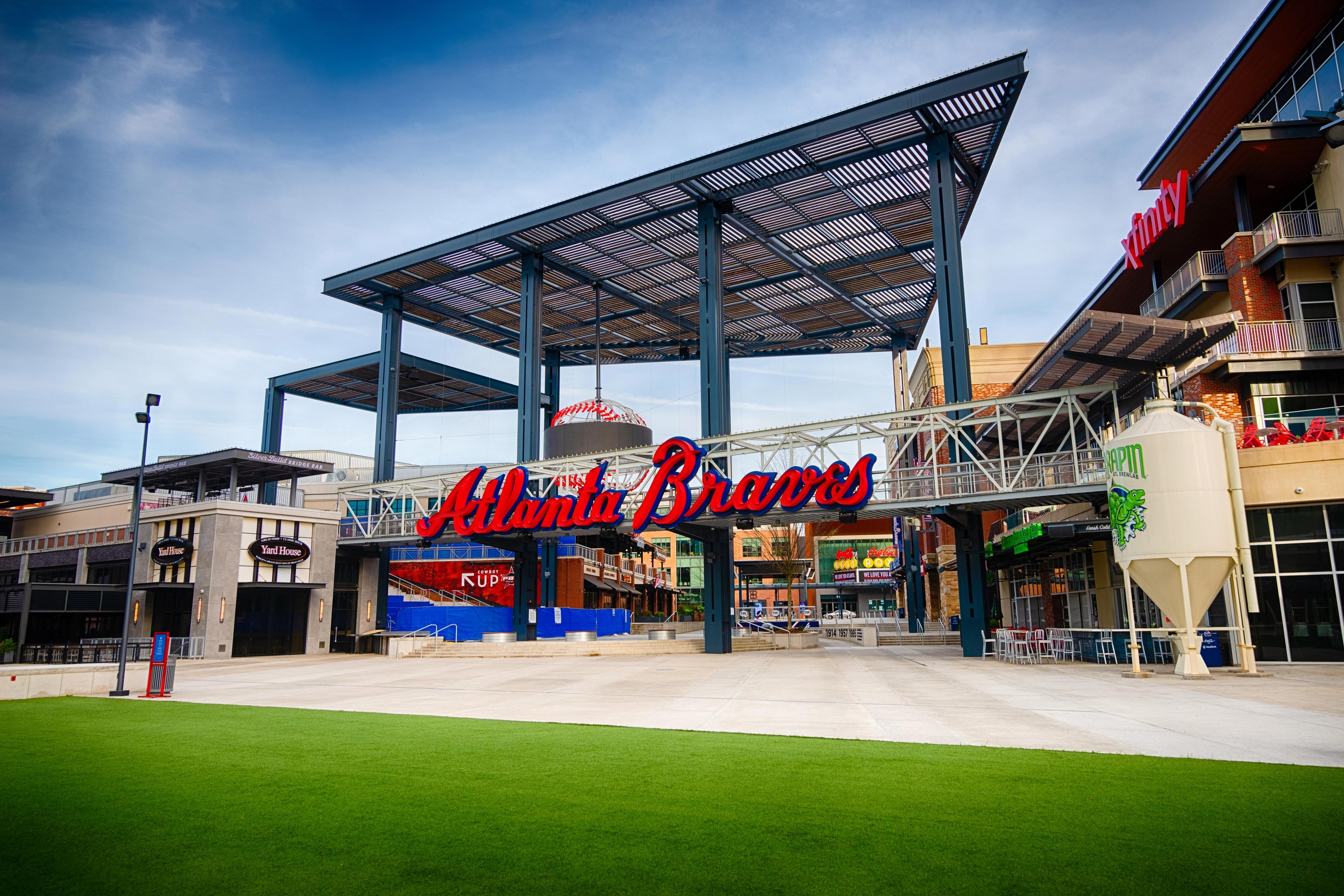 Atlanta Braves stadium entrance featuring iconic red sign, pedestrian bridge, and retail plaza with green turf in Marietta GA