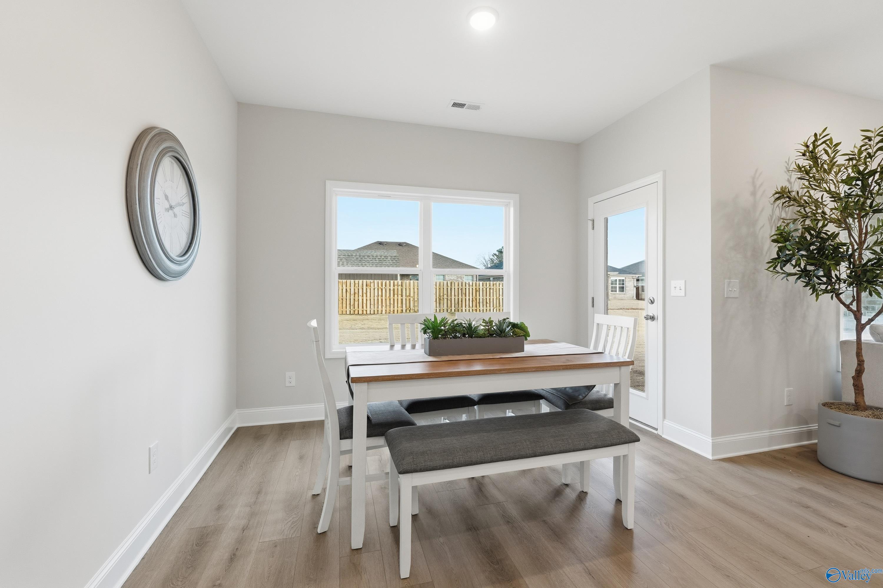 Bright dining nook with white rectangular table, gray bench seating, potted plants, and backyard view through large window in The Asheville home, Toney, Alabama