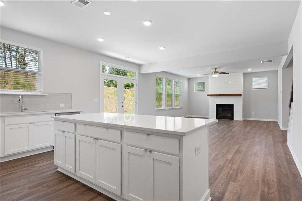 Modern open-concept kitchen with white island, farmhouse sink, and adjacent family room featuring gas fireplace in Davidson Homes The Hickory B, Winder, GA