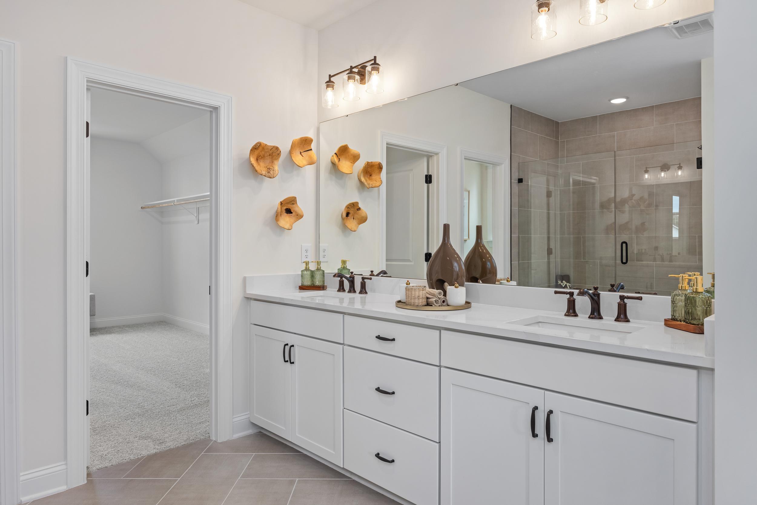 Spacious master bathroom at Laneridge Estates in Raleigh NC with white double vanity, frameless glass shower, and walk-in closet