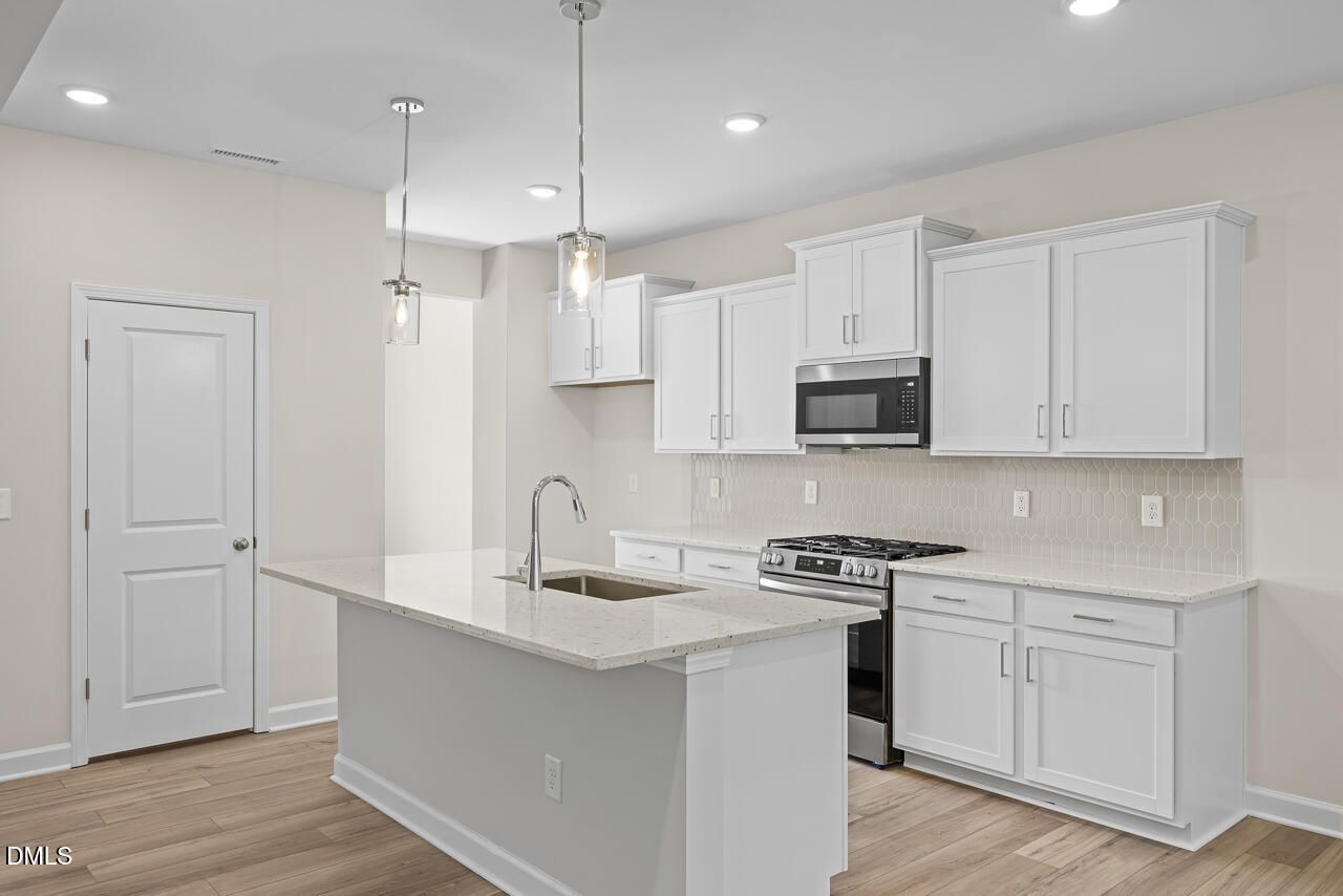 White kitchen with island, stainless gas range, and pendant lights in Davidson Homes The Willow C, Zebulon, NC