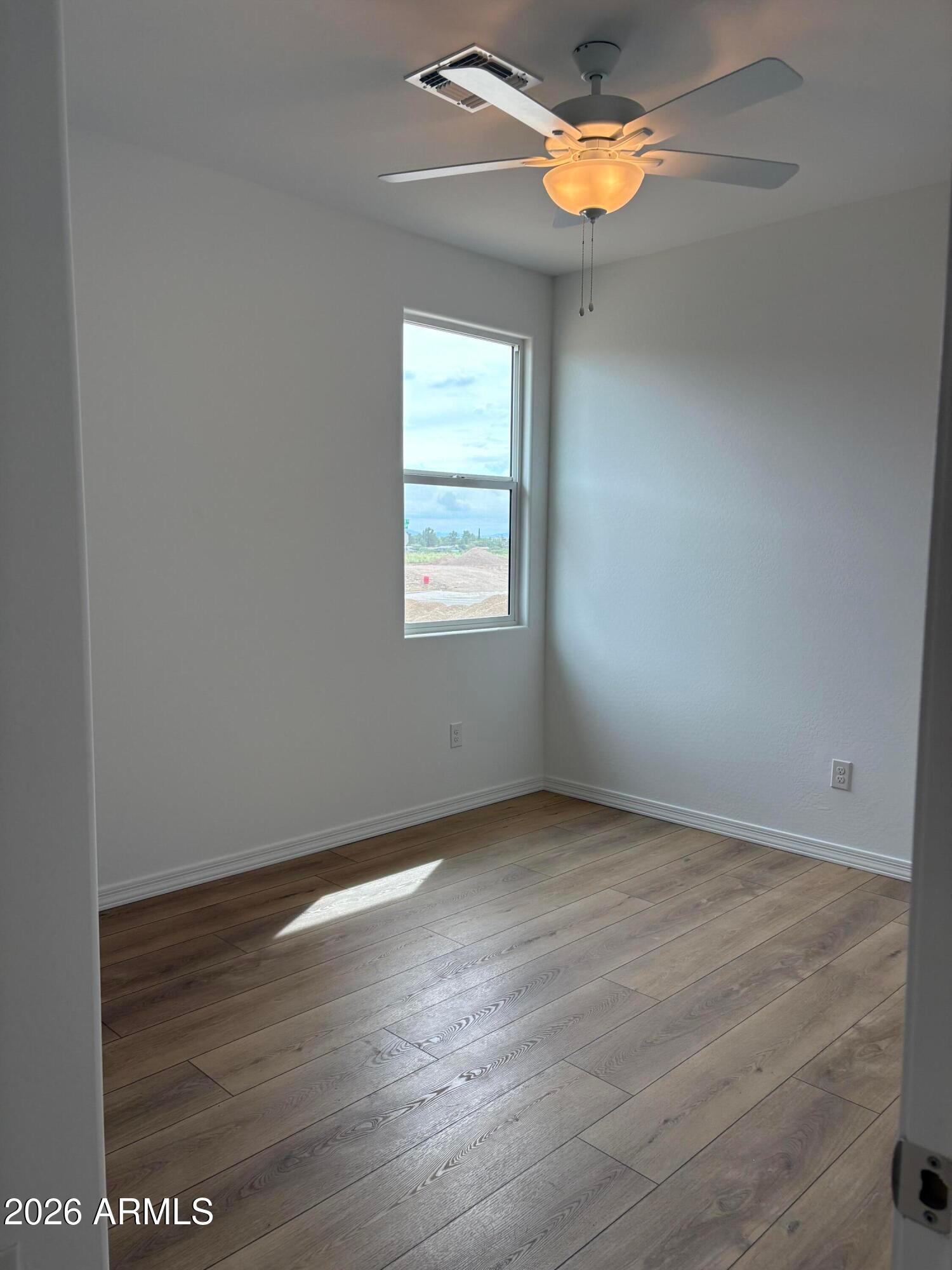 Bright empty bedroom with wood-look flooring, ceiling fan, and sunny window in Davidson Homes The Evergreen B, Cottonwood, Arizona