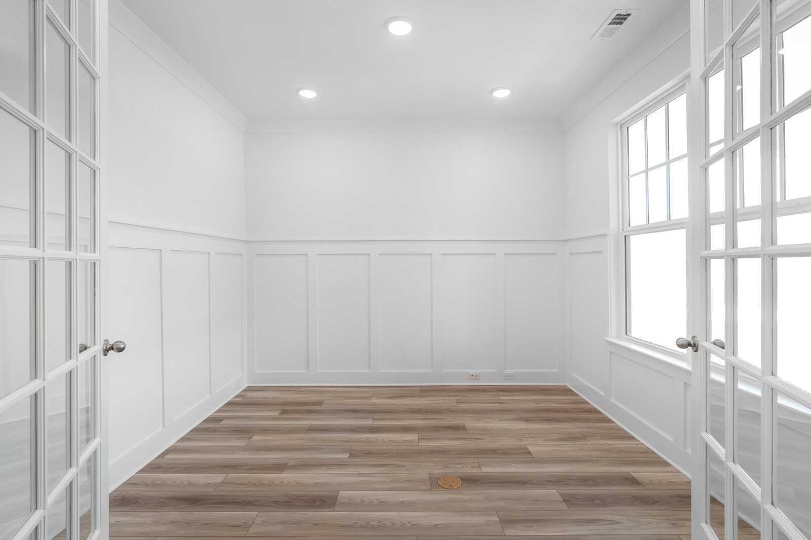 Bright empty room with white wainscot walls, open French doors, large window, recessed lights, and luxury vinyl plank flooring in Davidson Homes The Hathaway, Murfreesboro