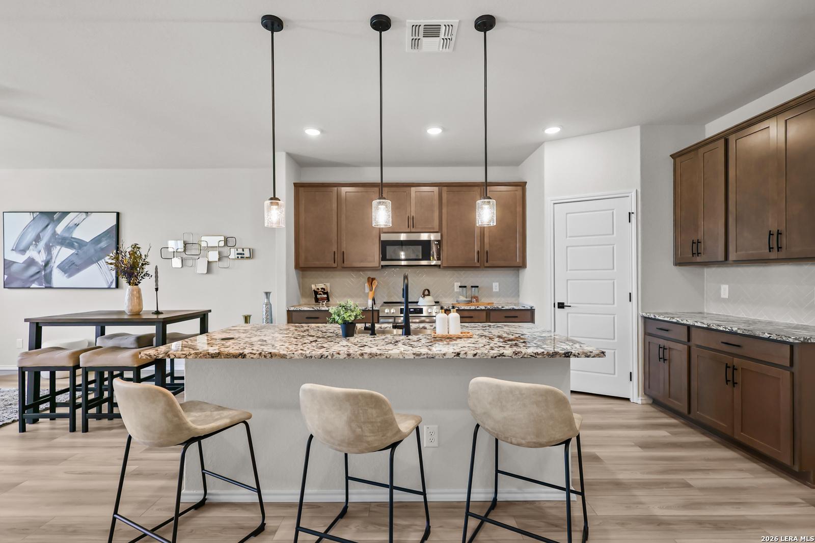 Modern kitchen with granite island, pendant lights, and dark wood cabinets in The Douglas C floor plan, Hannah Heights.